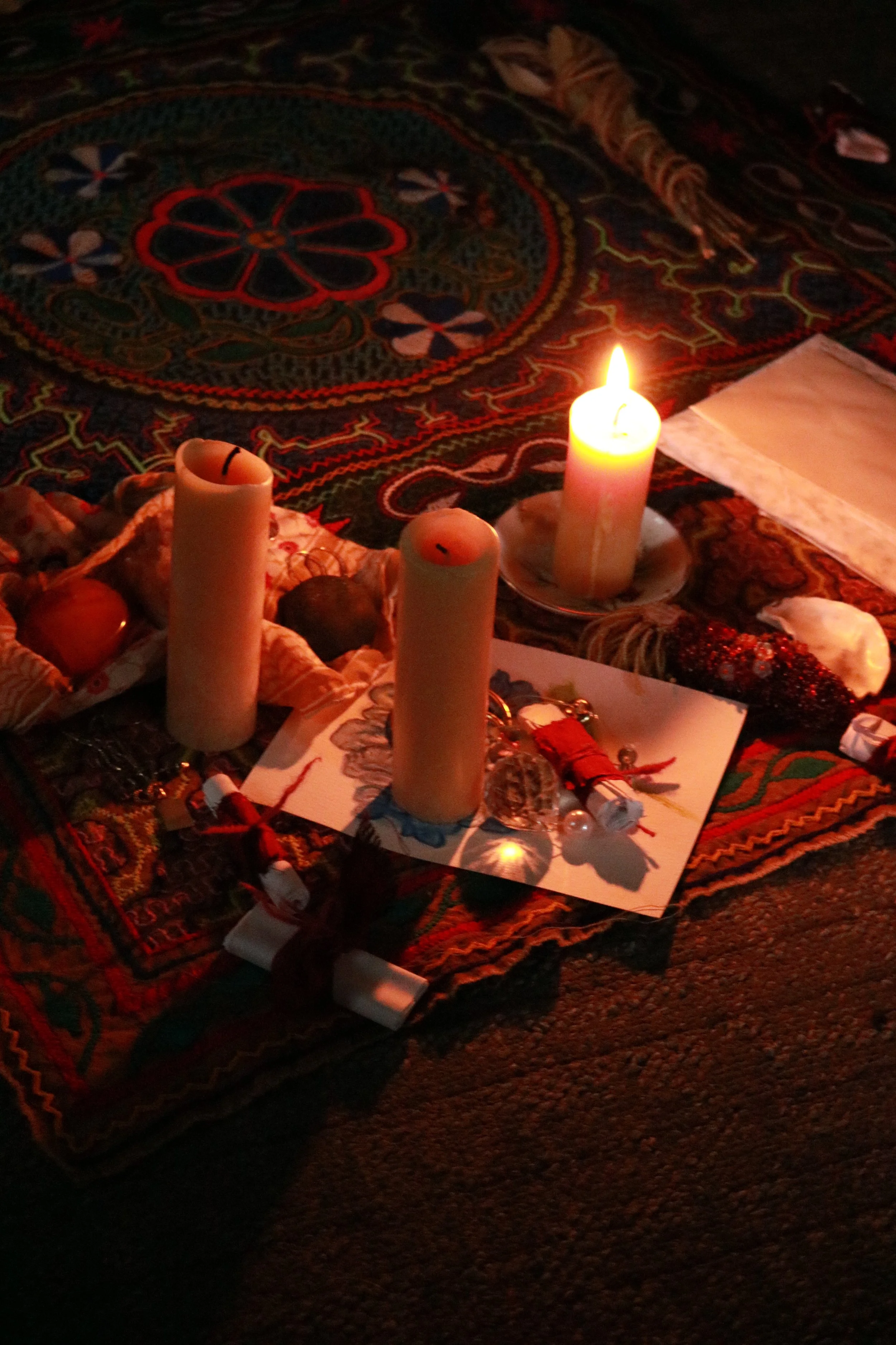 A candlelit ofrenda with candles, flowers, and small objects on a colorful, patterned cloth.