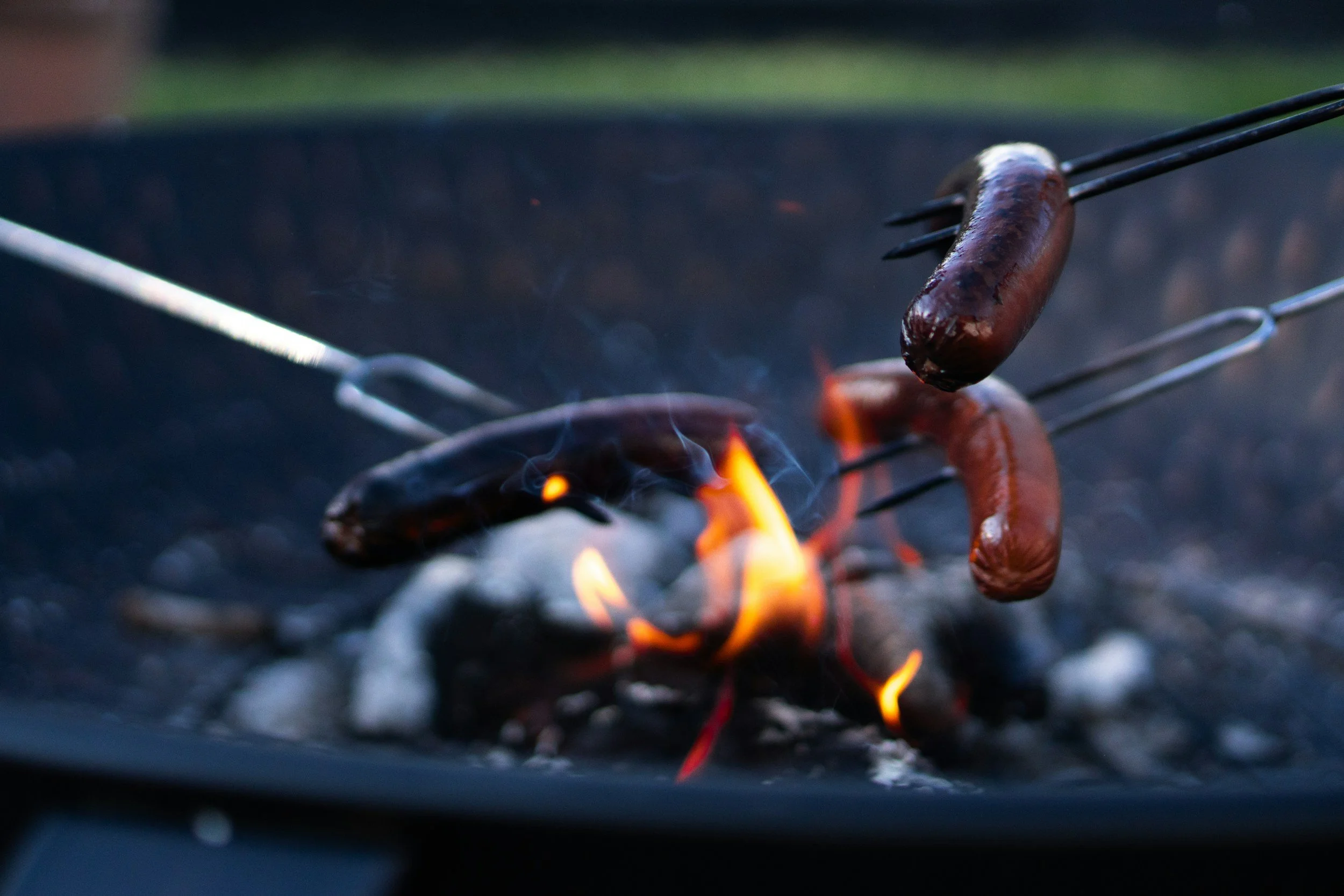 Sausages being grilled over an open flame with tongs in hand.