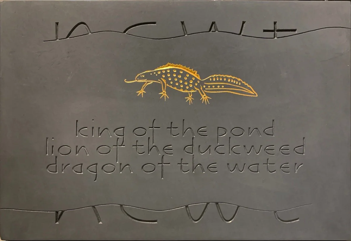 Metal plaque featuring an illustration of a salamander and engraved text that reads 'king of the pond, lion of the duckweed, dragon of the water.'