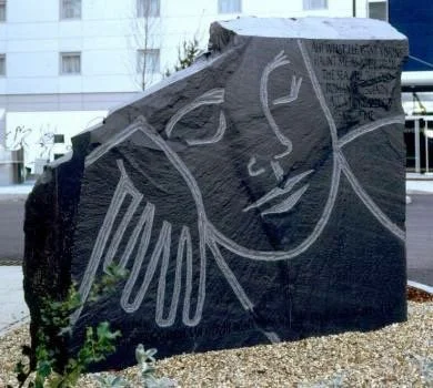 A large black rock with a white chalk drawing of a woman's face in a minimalist, abstract style.