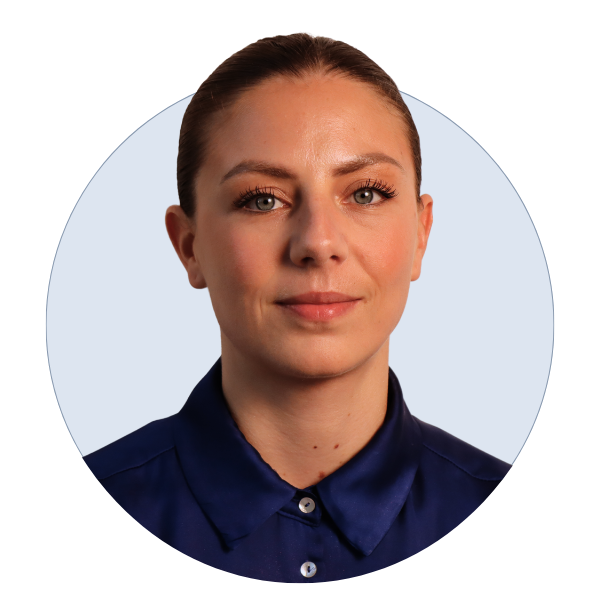 Headshot of a young woman with light skin and brown hair, wearing a navy blue collared shirt, looking at the camera with a neutral expression.