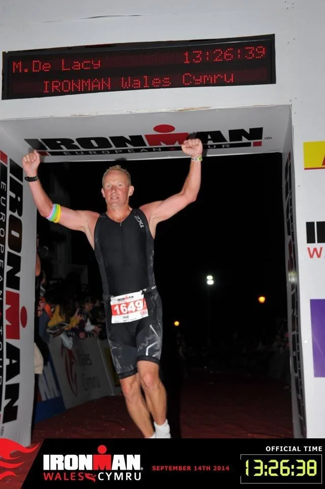 Male athlete crossing the finish line at the Ironman Wales triathlon in Cymru, Wales, on September 14th, 2014, celebrating his accomplishment with arms raised in victory.