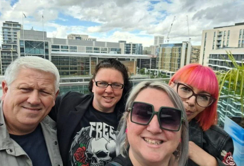 Four people smiling for a photo on a rooftop with city buildings in the background.