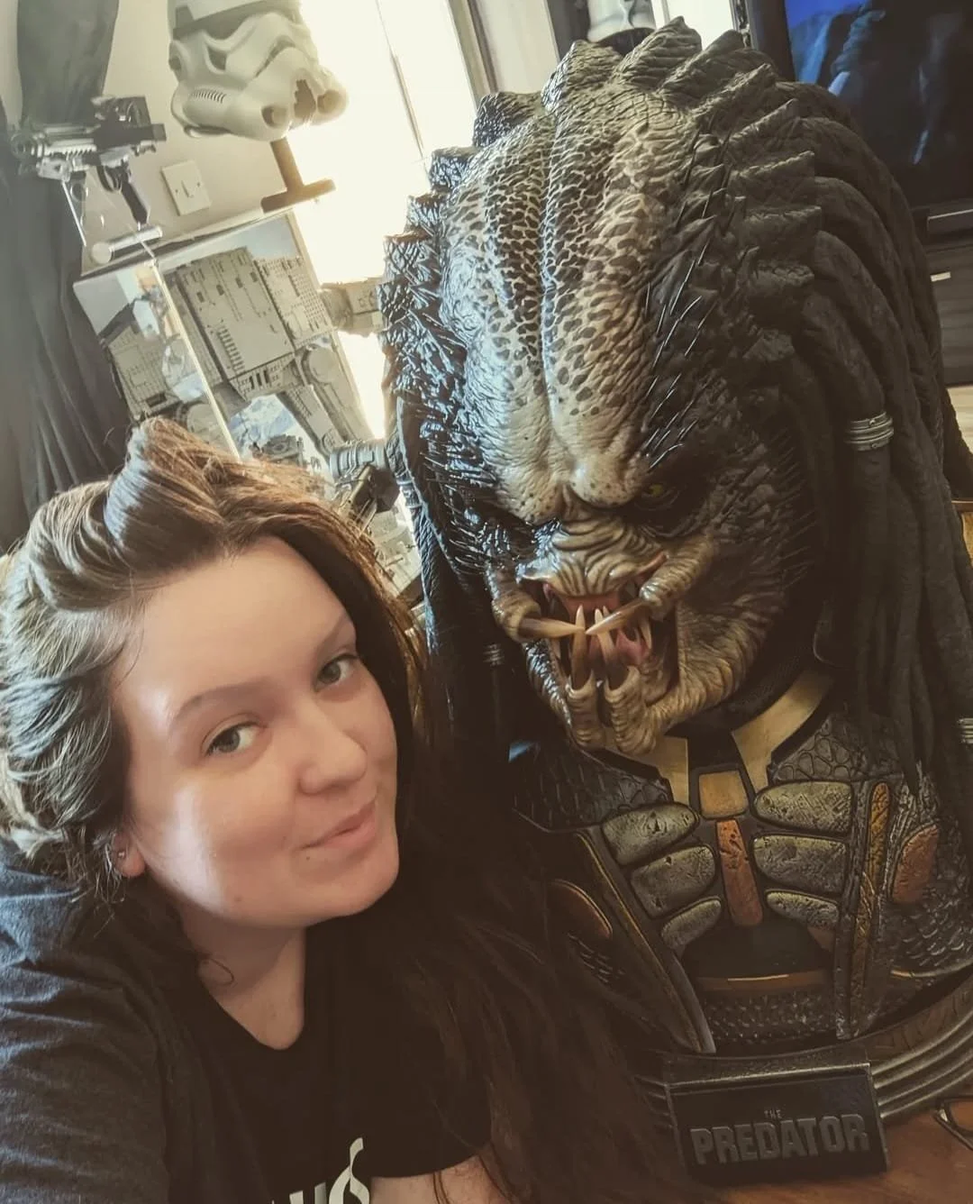 A woman taking a selfie with a life-sized Predator sculpture from the movie, showing the creature's detailed head and armor.
