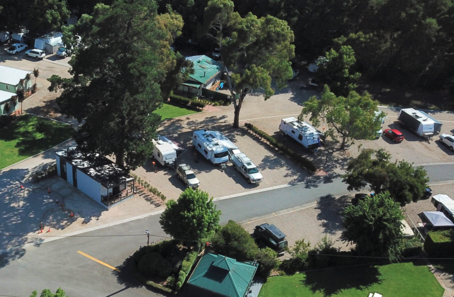 An aerial view of a parking lot with several RVs, caravans and cars, surrounded by trees and green spaces.