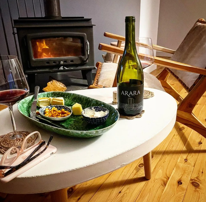 Bottle of Arara Wine on coffee table in front of lit fire with cheese platter and wine glasses