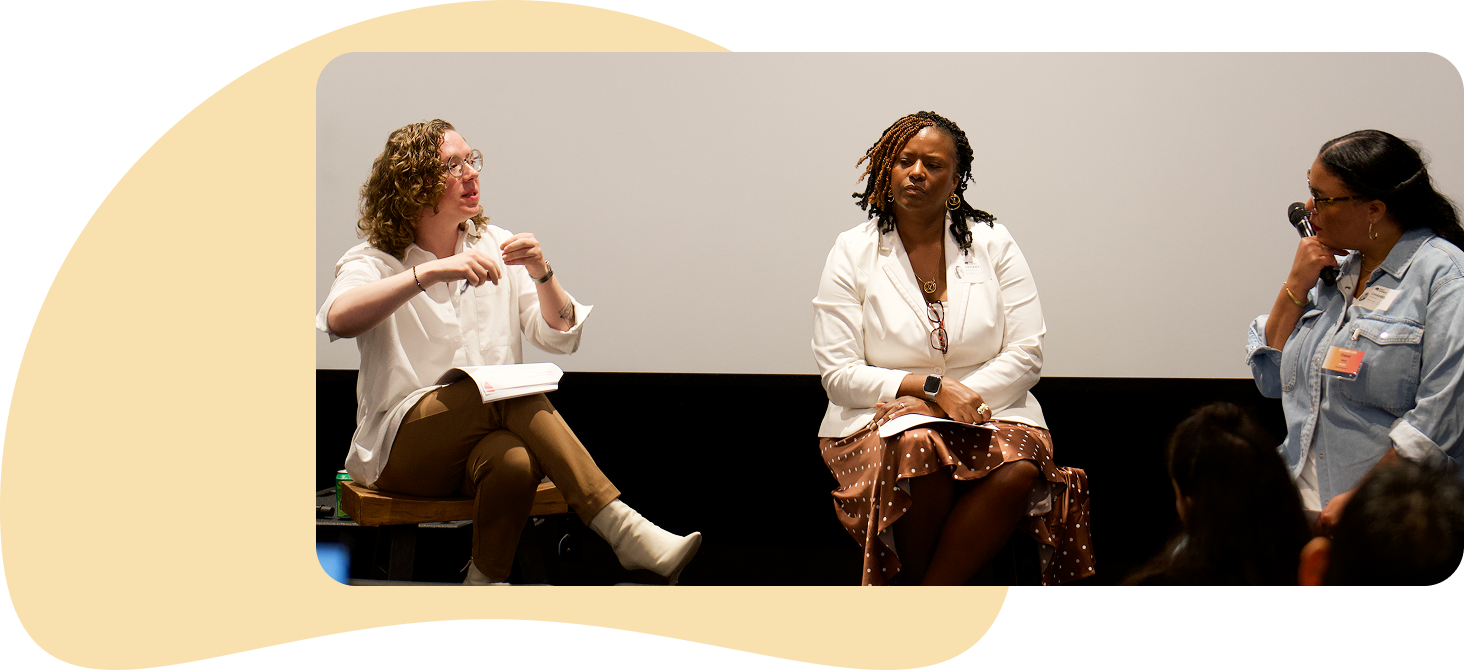 Three women sitting on a stage engaged in a panel discussion, with an audience in front of them.