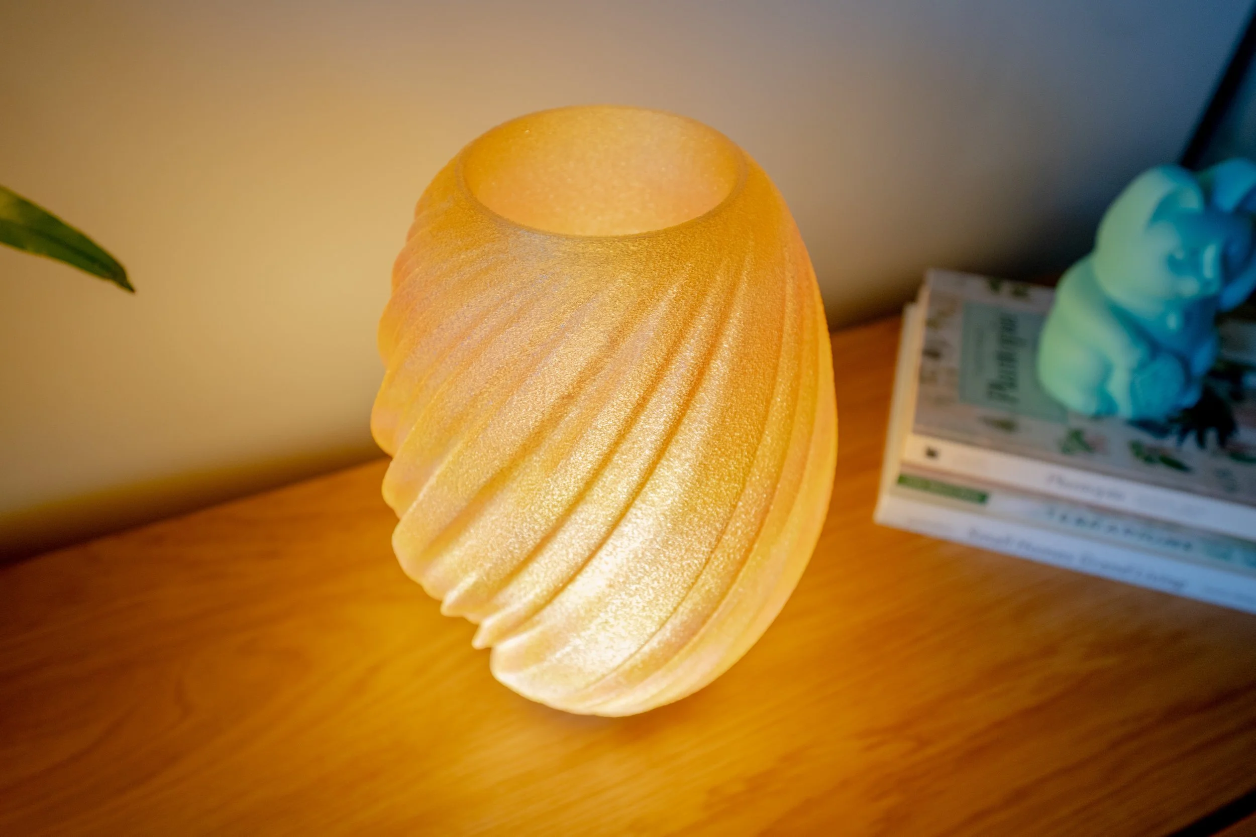 Yellow textured table 3d printed lamp on a wooden surface with stacked books and a small blue ceramic figurine of a lucky cat