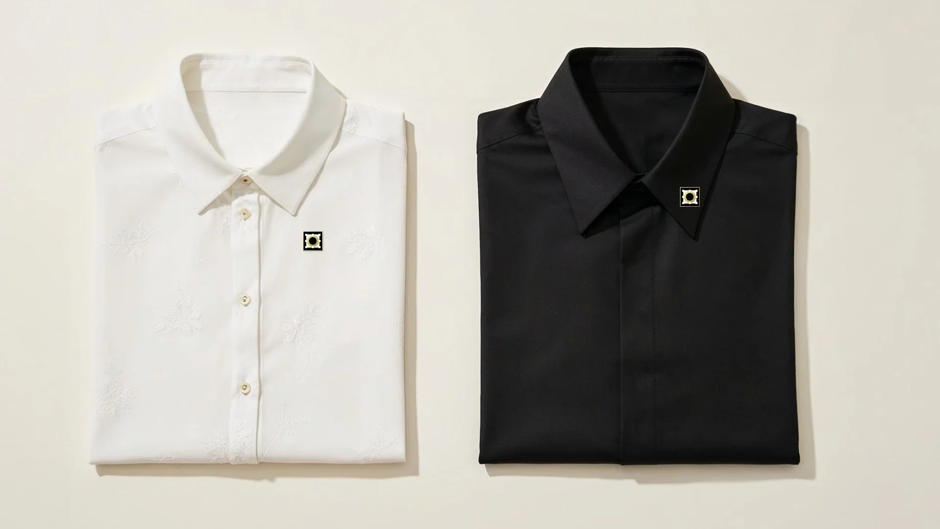 Twofold dress shirts, one white with floral embroidery and one black, neatly folded and displayed side by side on a plain background.