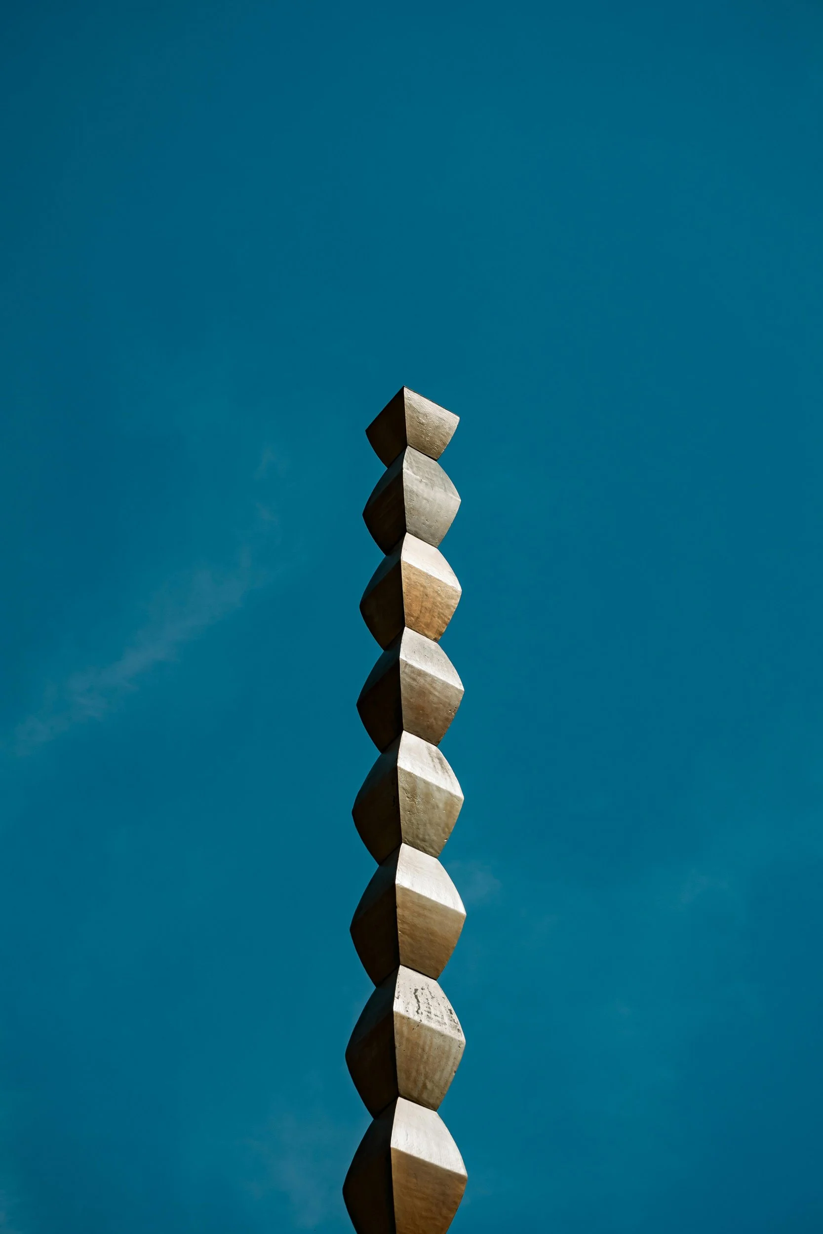 Ein vertikal ausgerichteter, skulpturaler Kunstblock aus mehreren weißen, kubischen Elementen gegen den blauen Himmel.