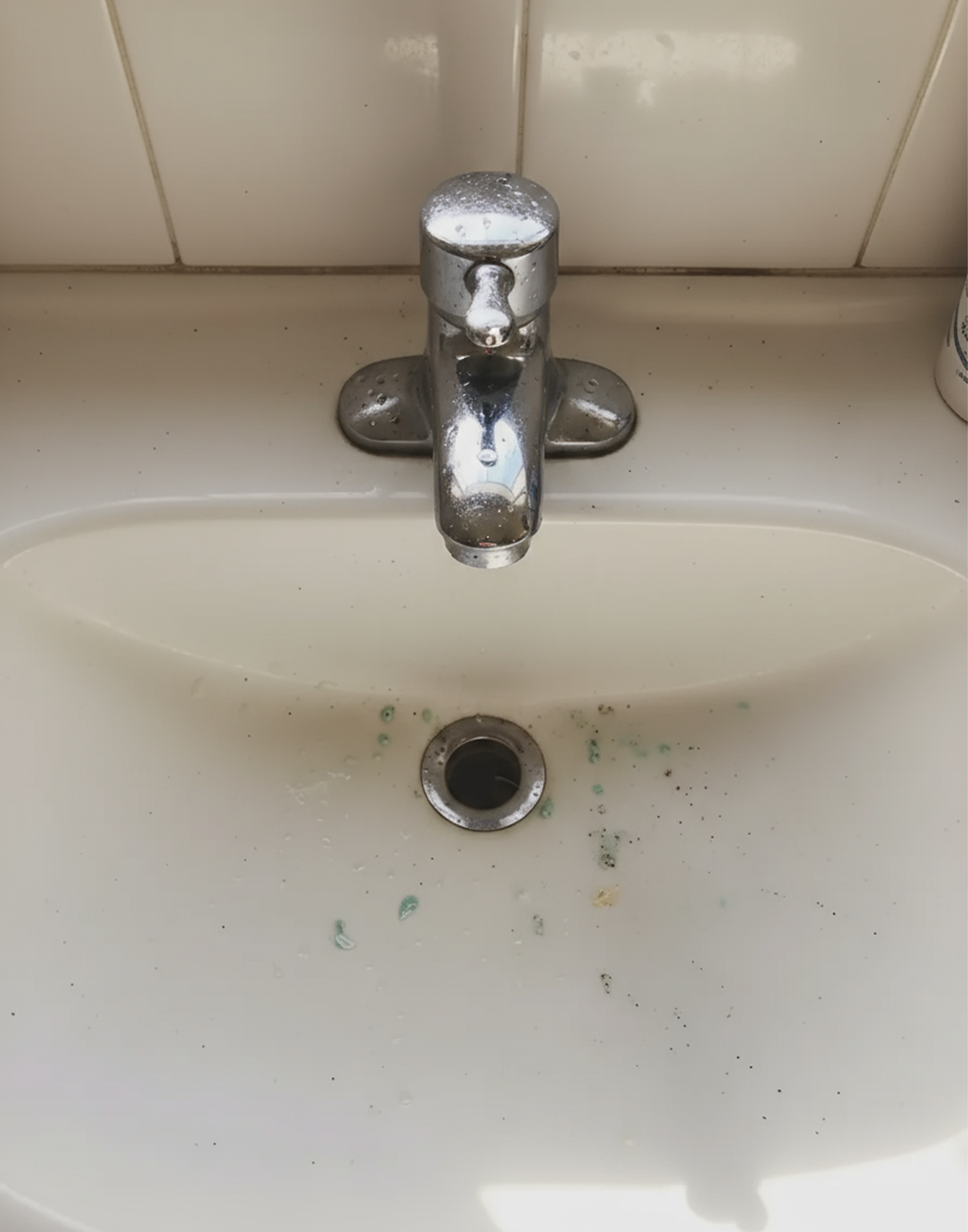 En vit handfat med en kromad handtork och ett handfat-filter, smutsiga munstycken och avlagringar i vasken.