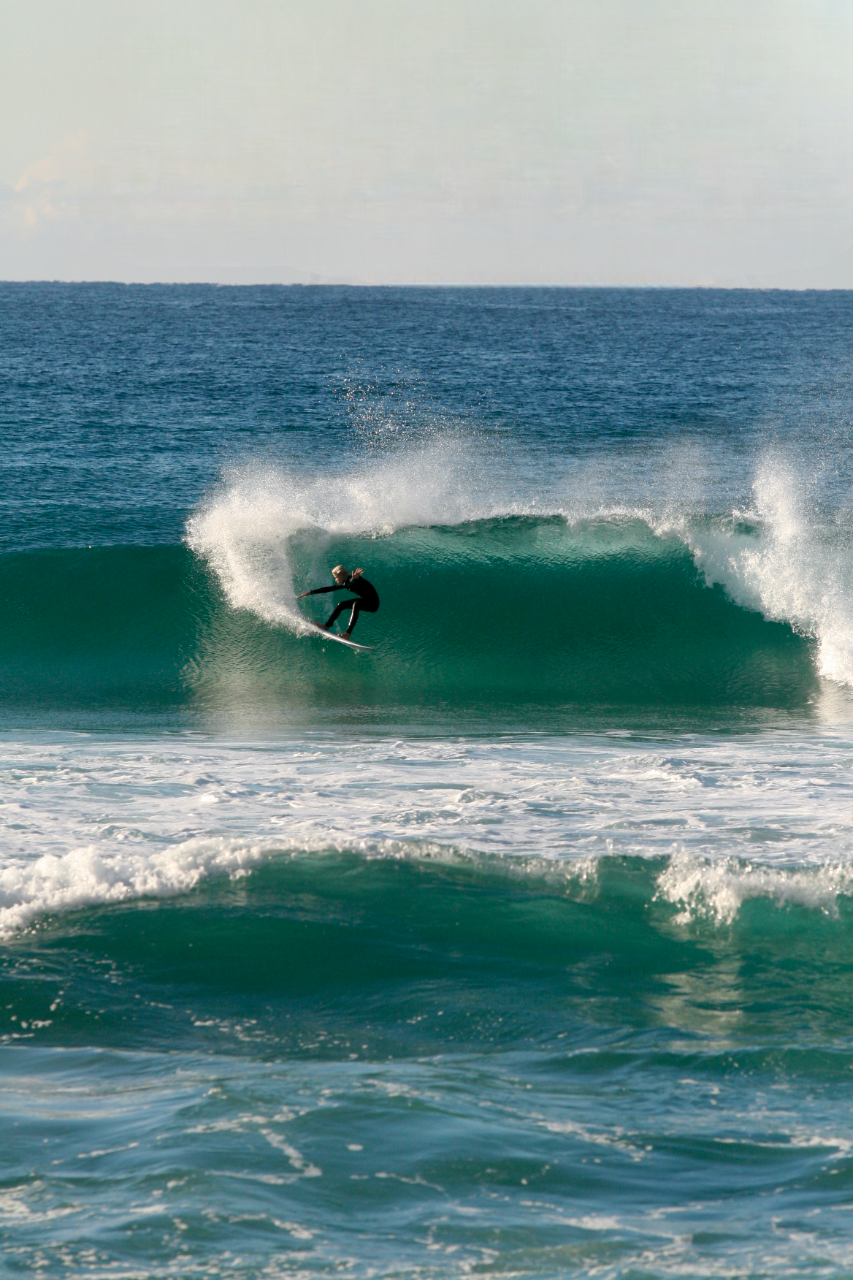 A surfer riding a large wave in the ocean with a clear sky in the background.