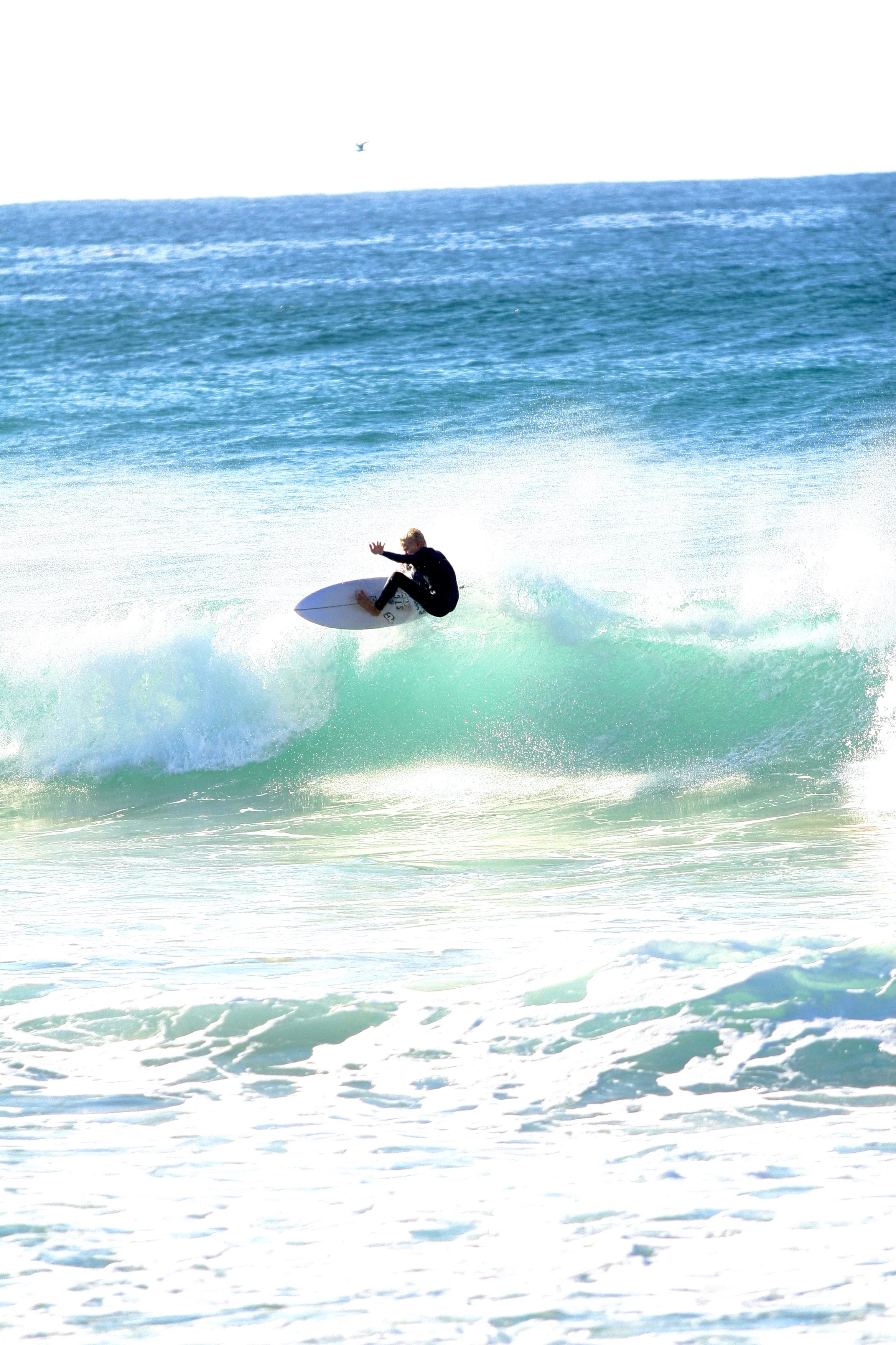 A person surfing on a wave in the ocean with blue water and white foam.