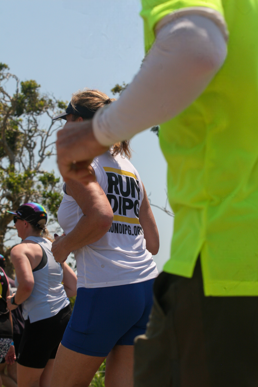 Group of runners wearing athletic gear and race shirts at an outdoor event on a sunny day.