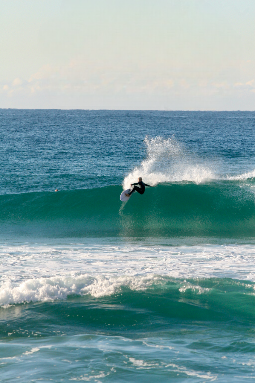 A person in a wetsuit riding a wave on a surfboard at the beach.