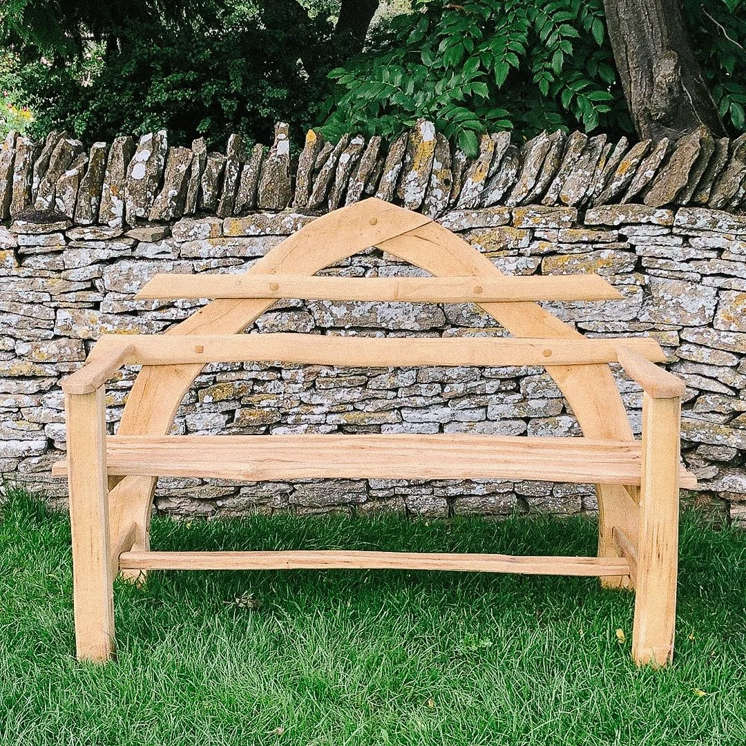 wooden garden bench in front of stone wall with green foliage.