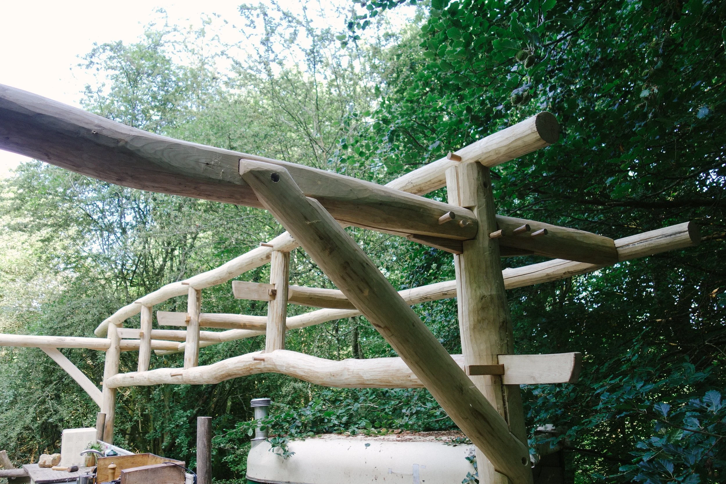 Unfinished wooden railing structure built in a forested area with trees and foliage in the background.