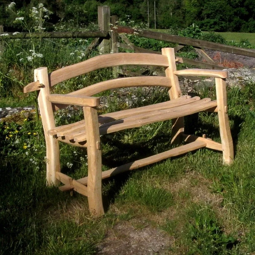 wooden garden bench outdoors on grass with a rustic fence and green foliage in the background.