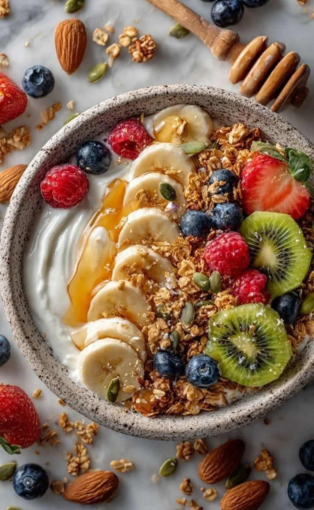 A bowl of yogurt topped with bananas, blueberries, strawberries, kiwi, granola, and pumpkin seeds, with honey drizzled on top.