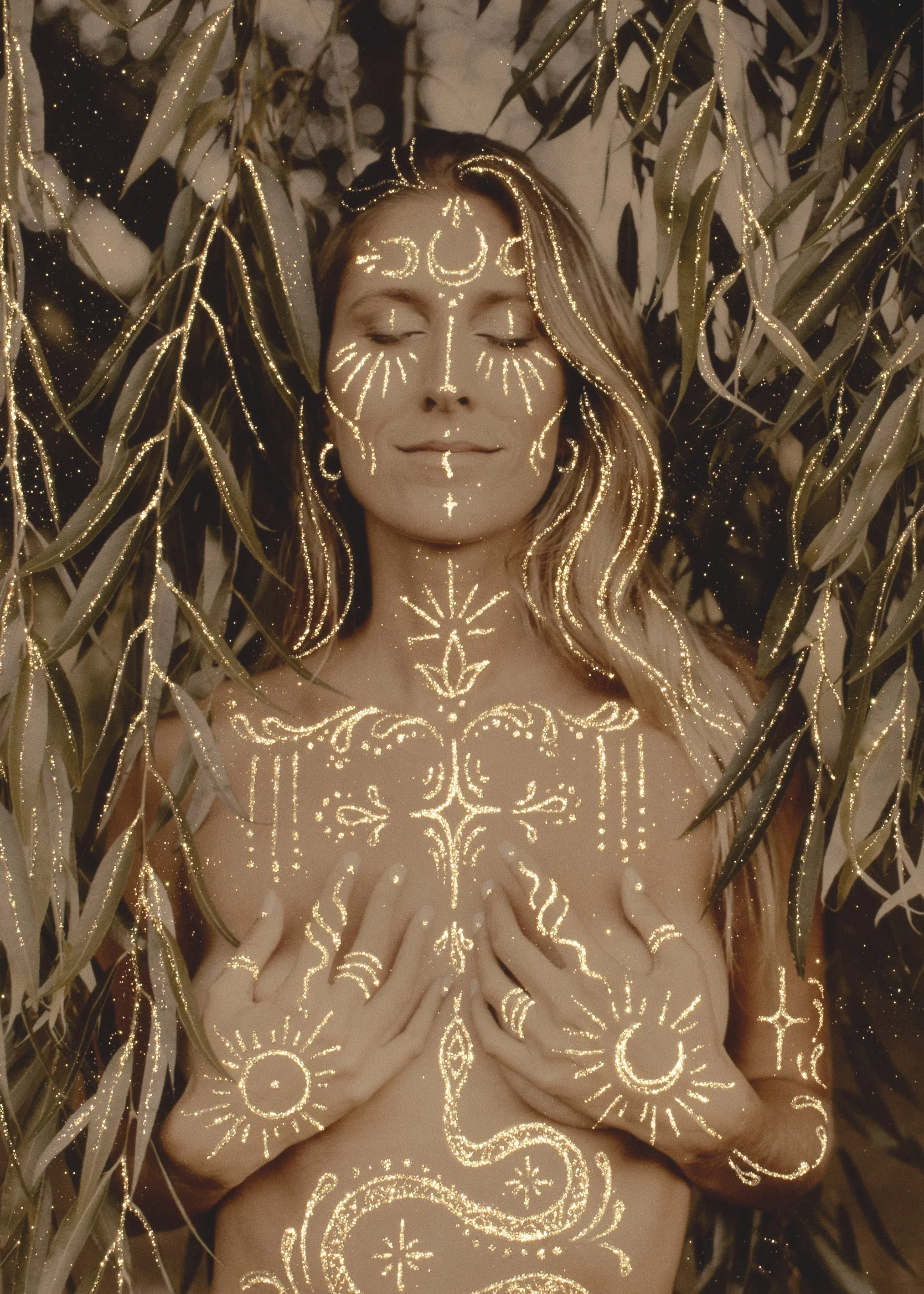 Una mujer con ojos cerrados rodeada de plantas, con tatuajes brillantes y decorativos en su cara y cuerpo que parecen ser de luz o brillo dorado.