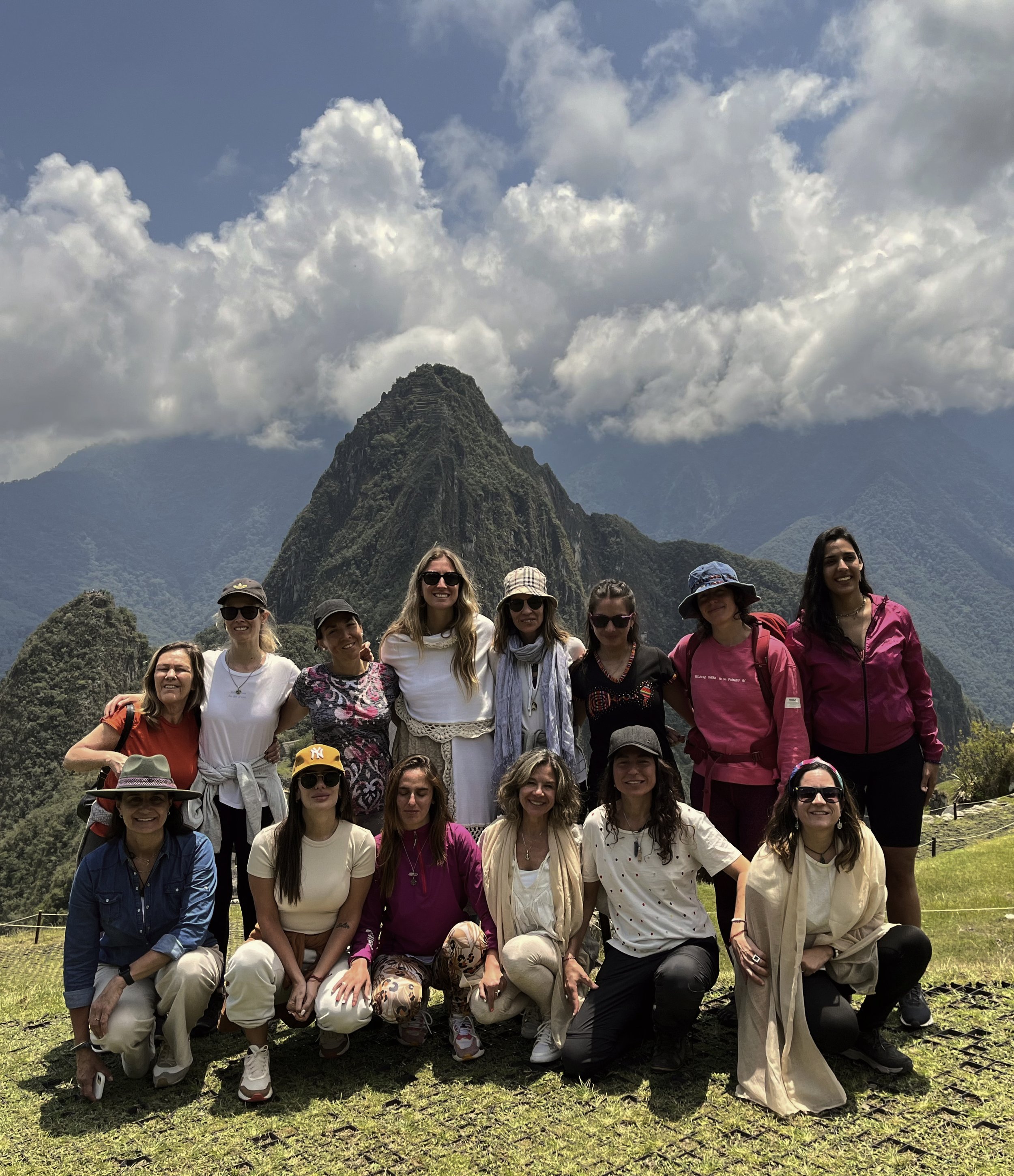Grupo de mujeres jóvenes posando en Machu Picchu, con montañas y nubes en el fondo.
