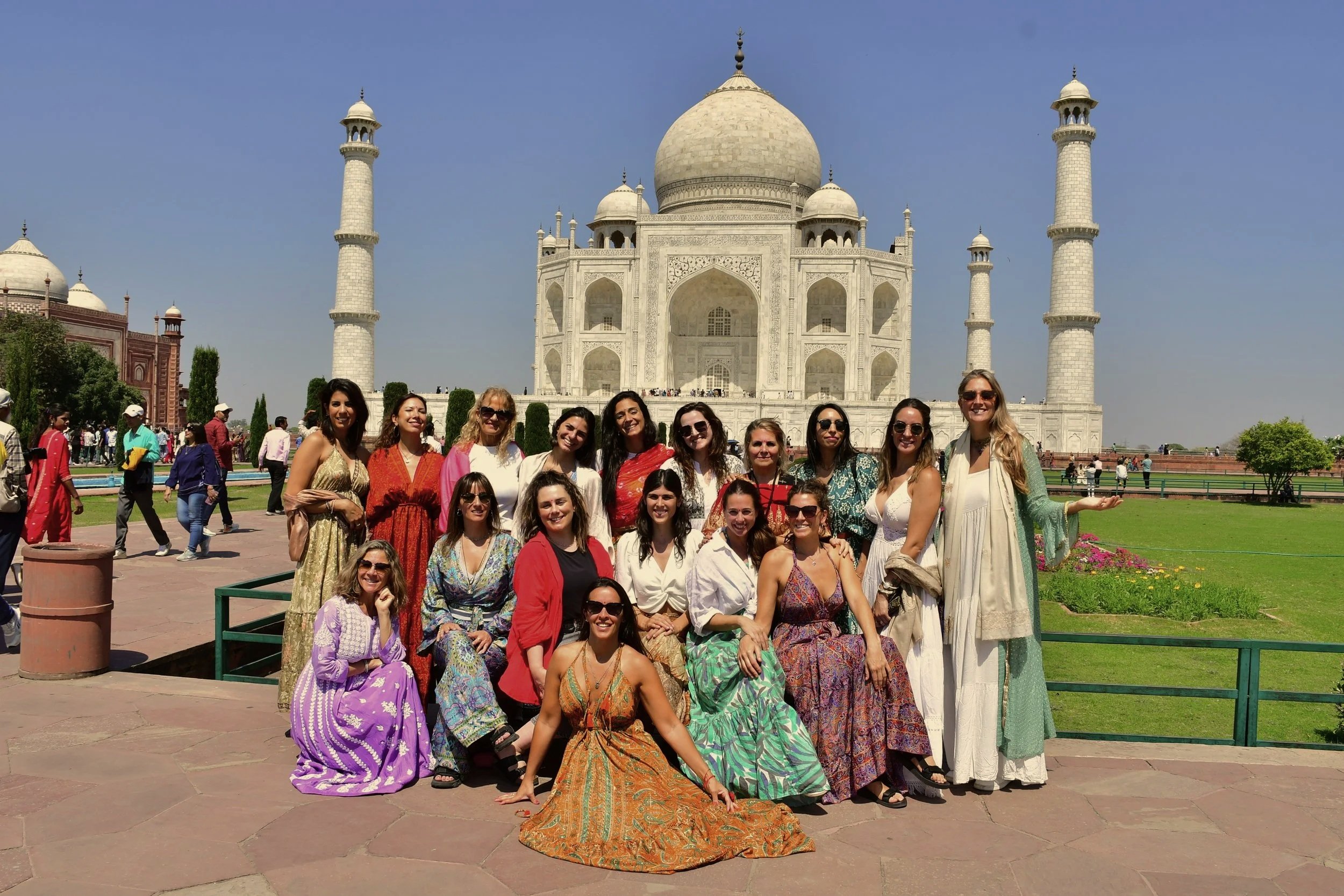 Grupo de personas posando frente al Taj Mahal en India, con ropa colorida y sonriendo en un día soleado.