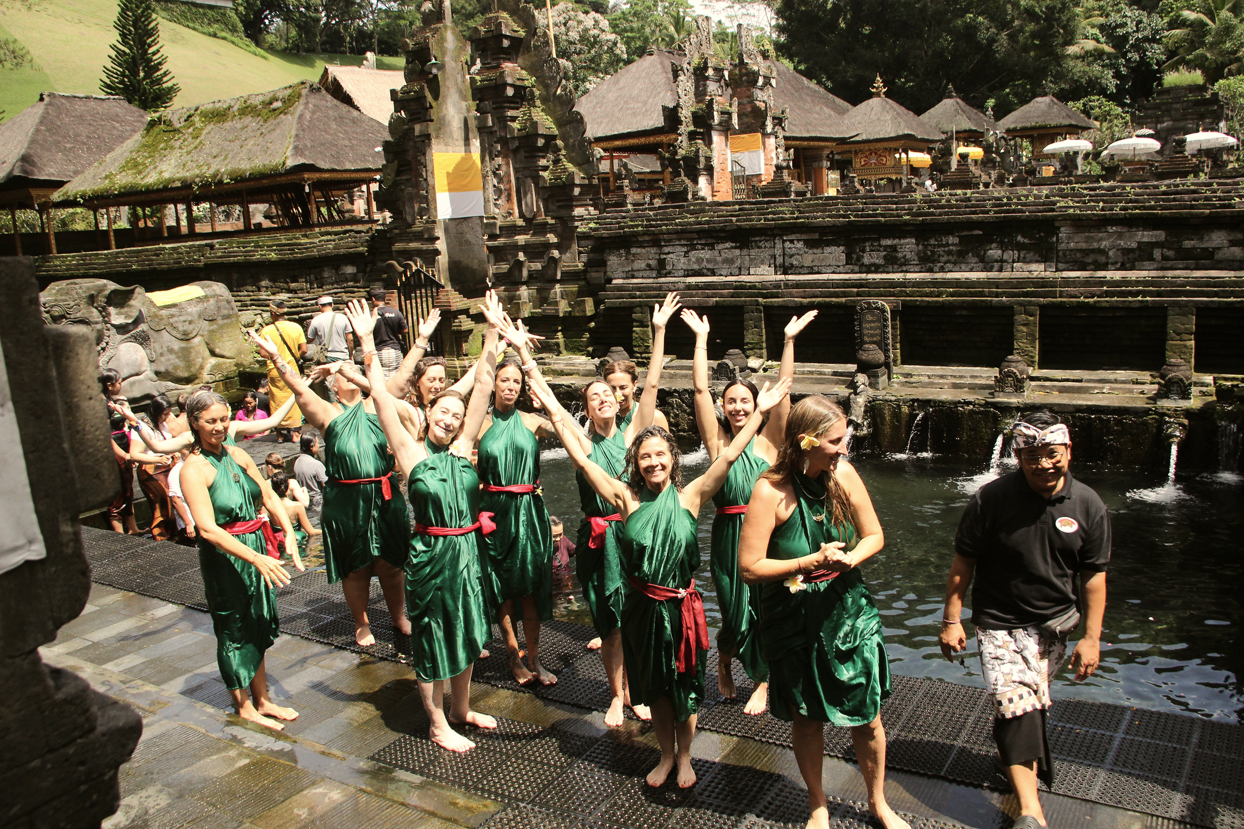 Grupo de mujeres bailando en un río frente a un templo antiguo de piedra, en un entorno natural con vegetación.