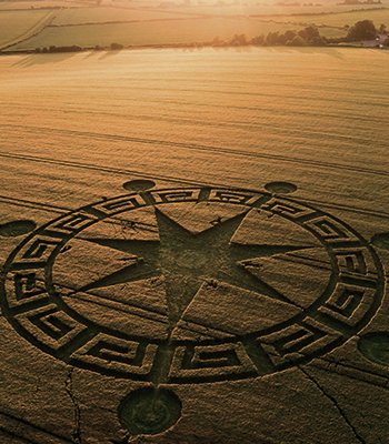 Crop circle en forma de compás en un campo de cereales bajo cielo soleado