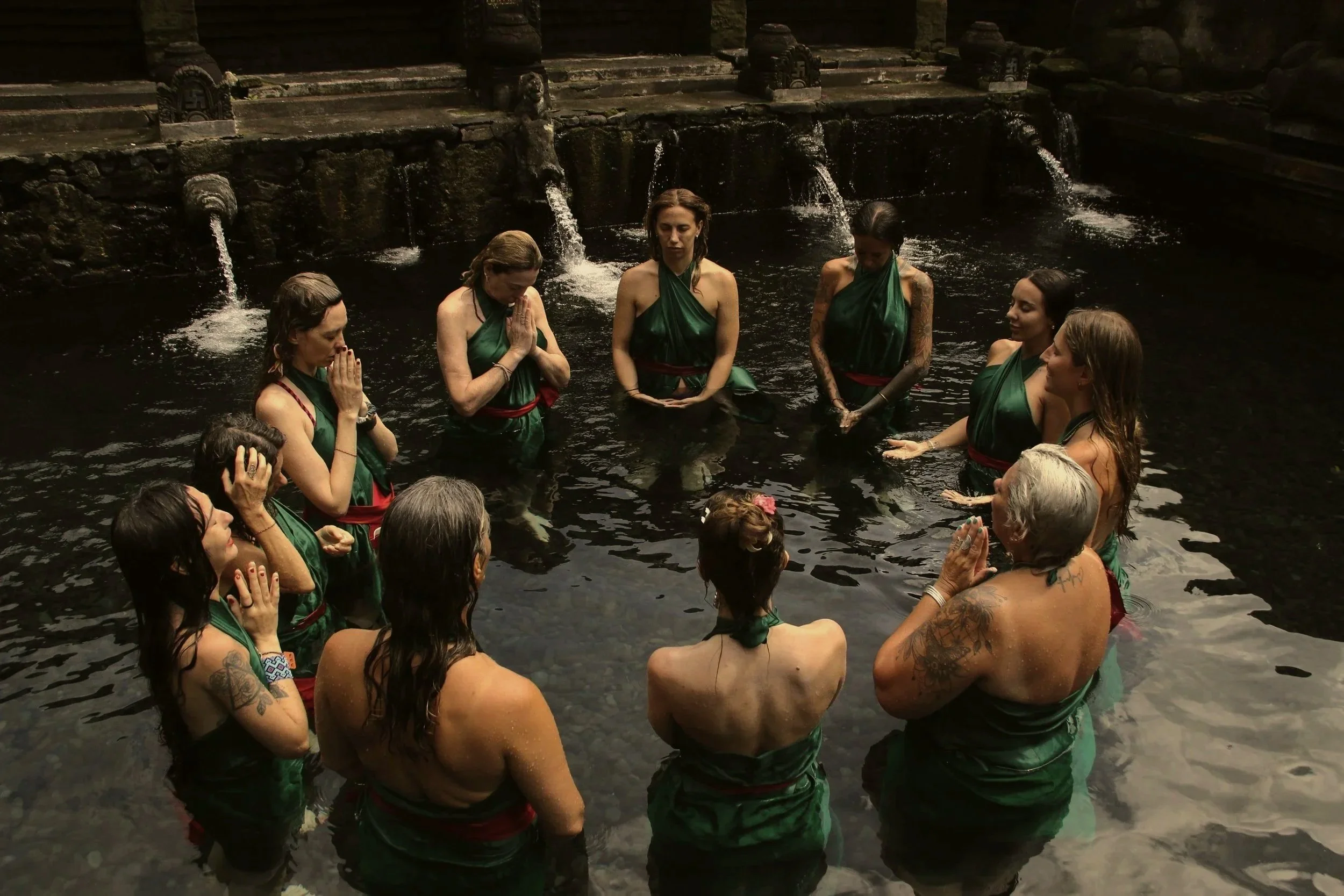 Grupo de personas realizando un ritual en un río o fountain, con las manos juntas en oración, rodeados de agua y piedra.