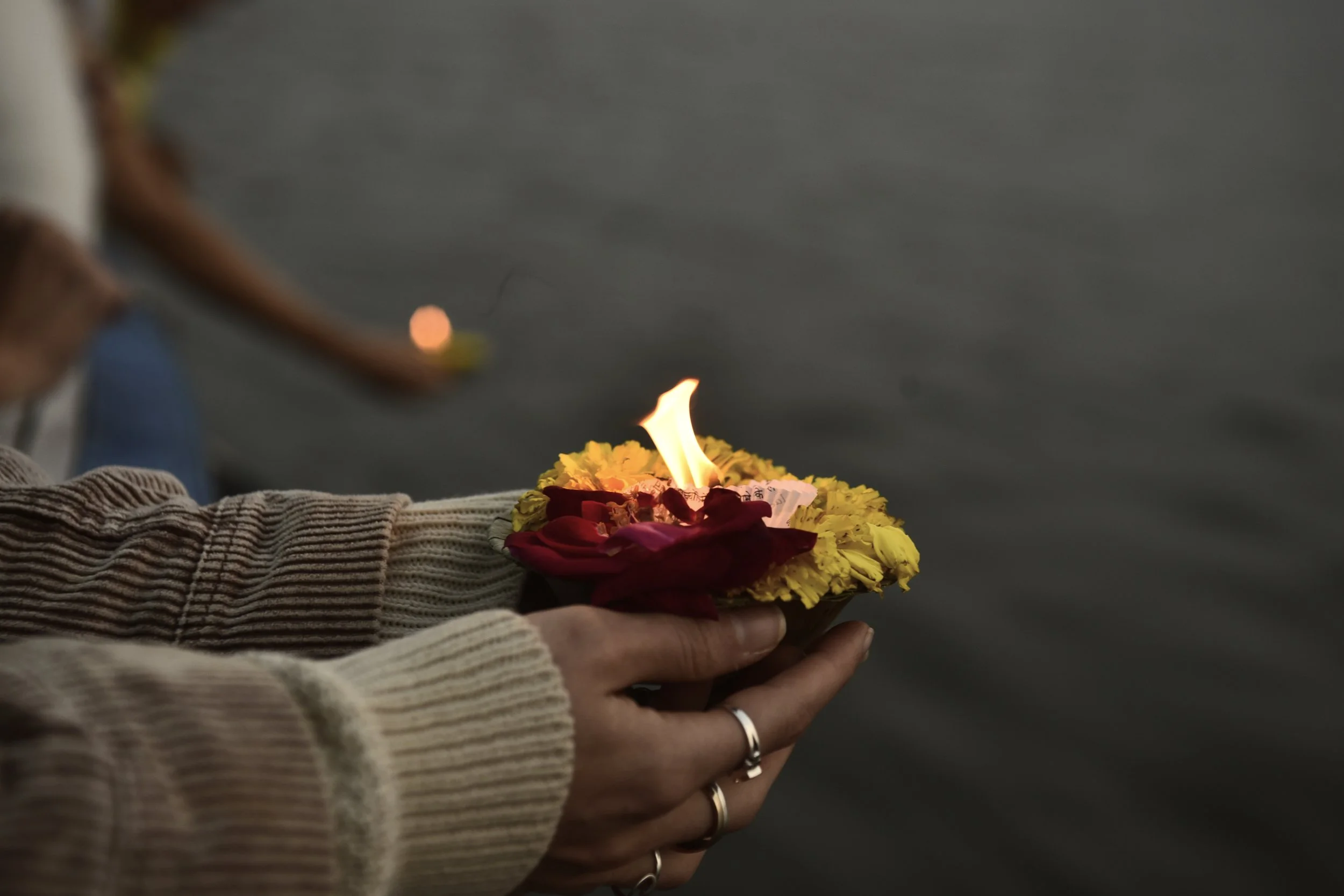Persona sosteniendo un altar ceremonial con una llama en un entorno acuático, rodeada de flores en tonos rojos y amarillos