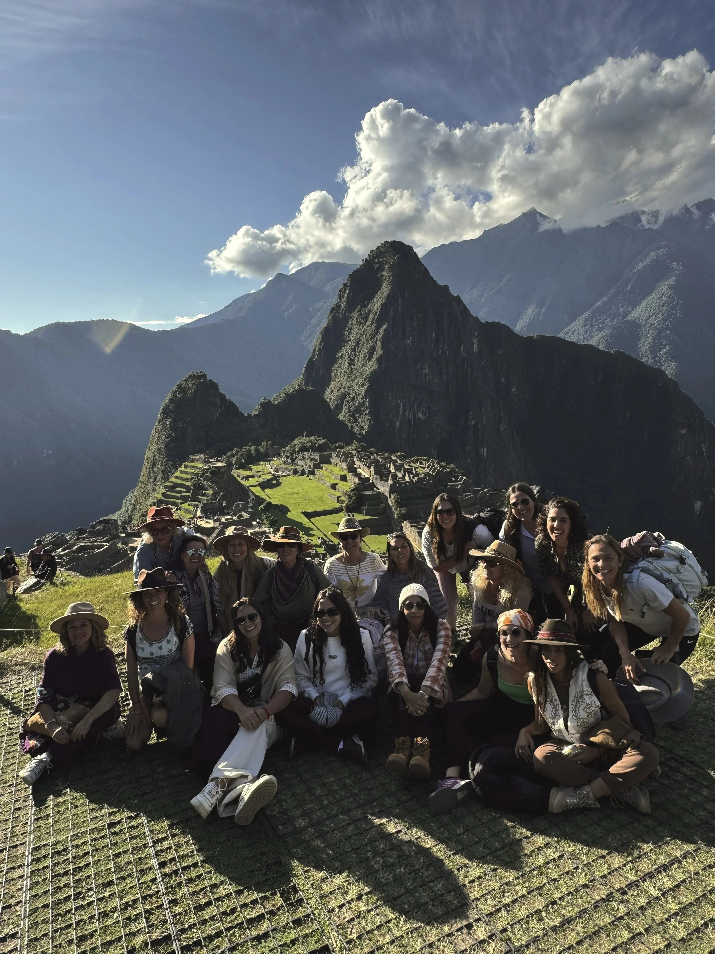 Grupo de personas posando en Machu Picchu con las montañas y pirámides en el fondo, durante el día.