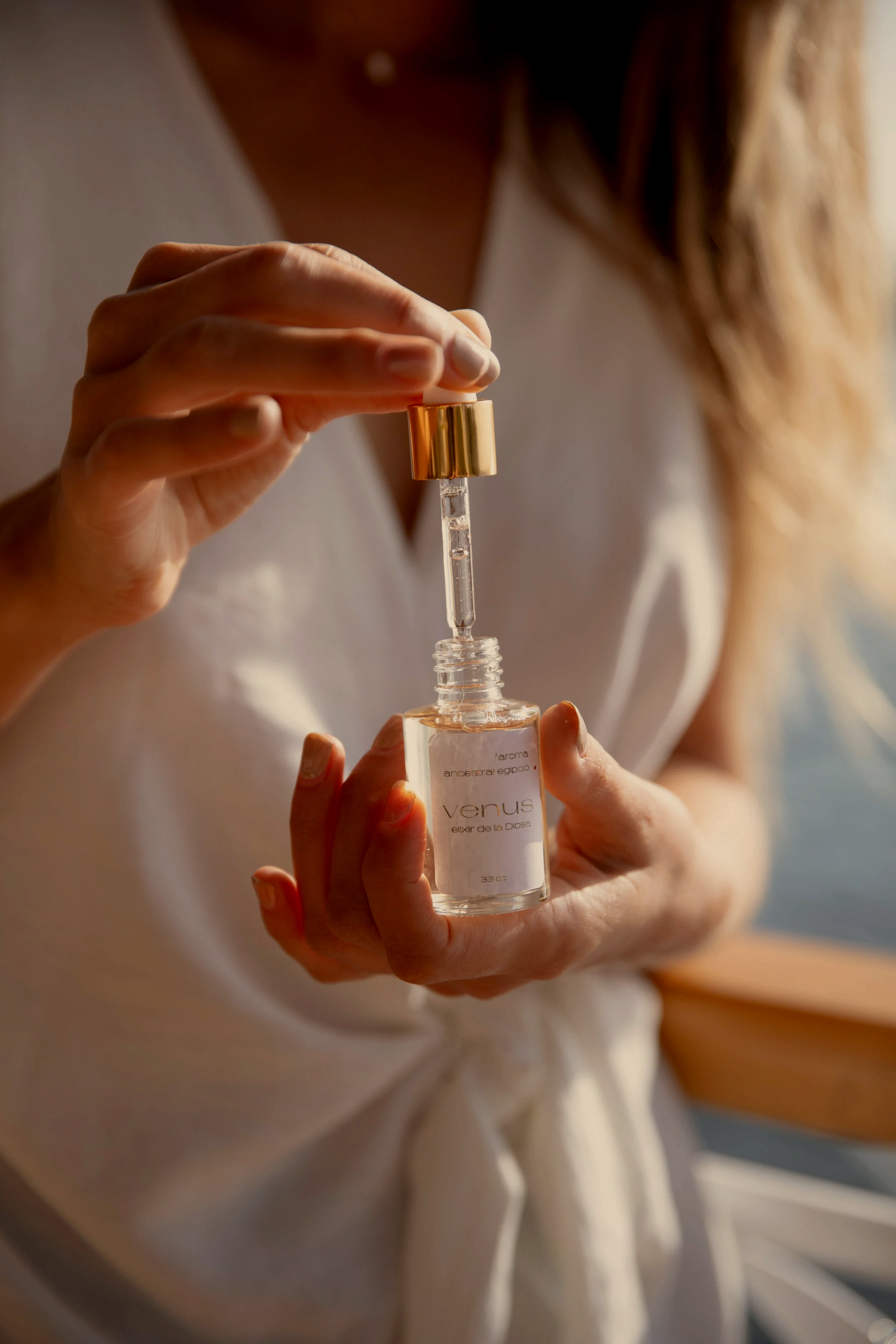 Persona sosteniendo un frasco de aceite esencial con gotero, etiquetado como Venus, en un ambiente con luz natural.