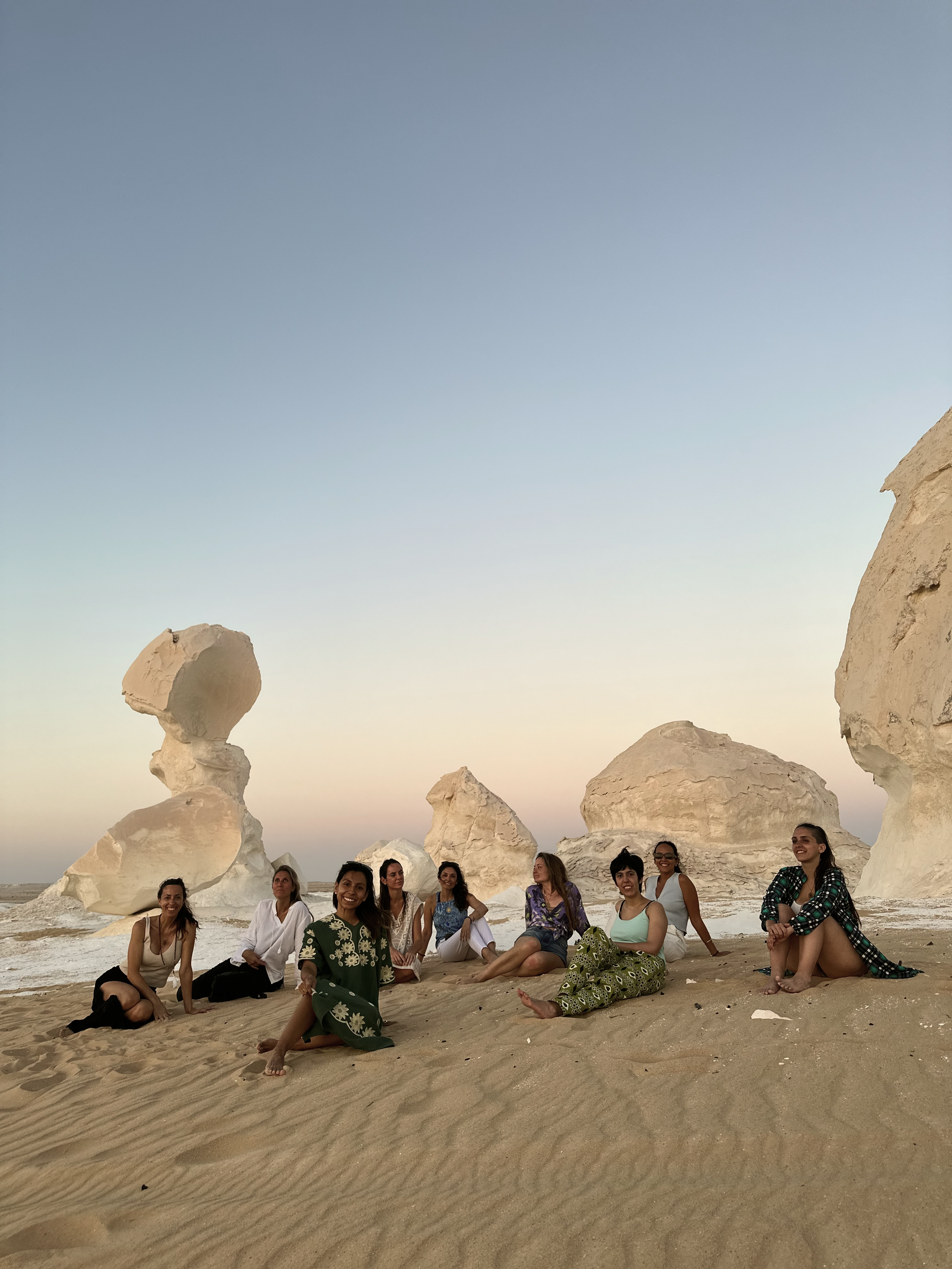 Grupo de personas disfrutando en la playa con formaciones rocosas en el fondo durante el atardecer.