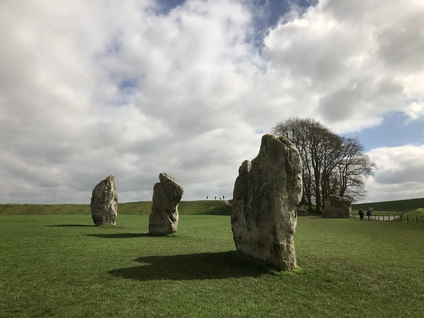 Tres antiguas piedras grandes en un campo verde con árboles y un cielo nublado.