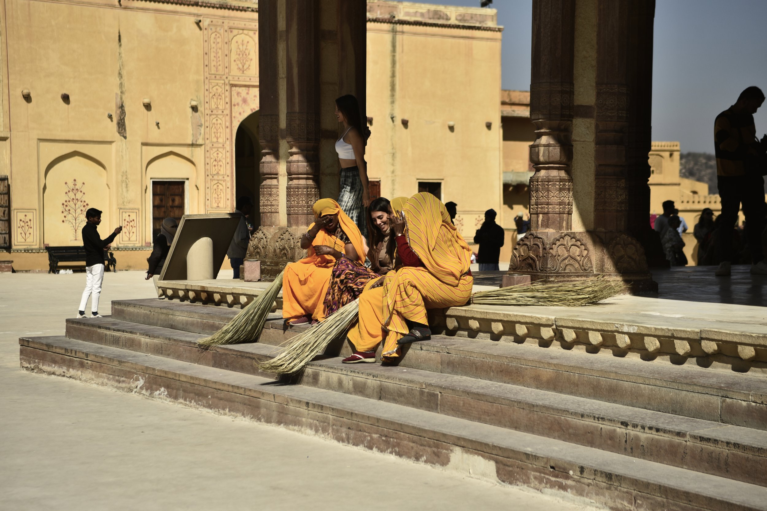 Personas en coloridos ropajes en un sitio histórico con arquitectura antigua y columnas de piedra, algunas en sombra y otras expuestas al sol.