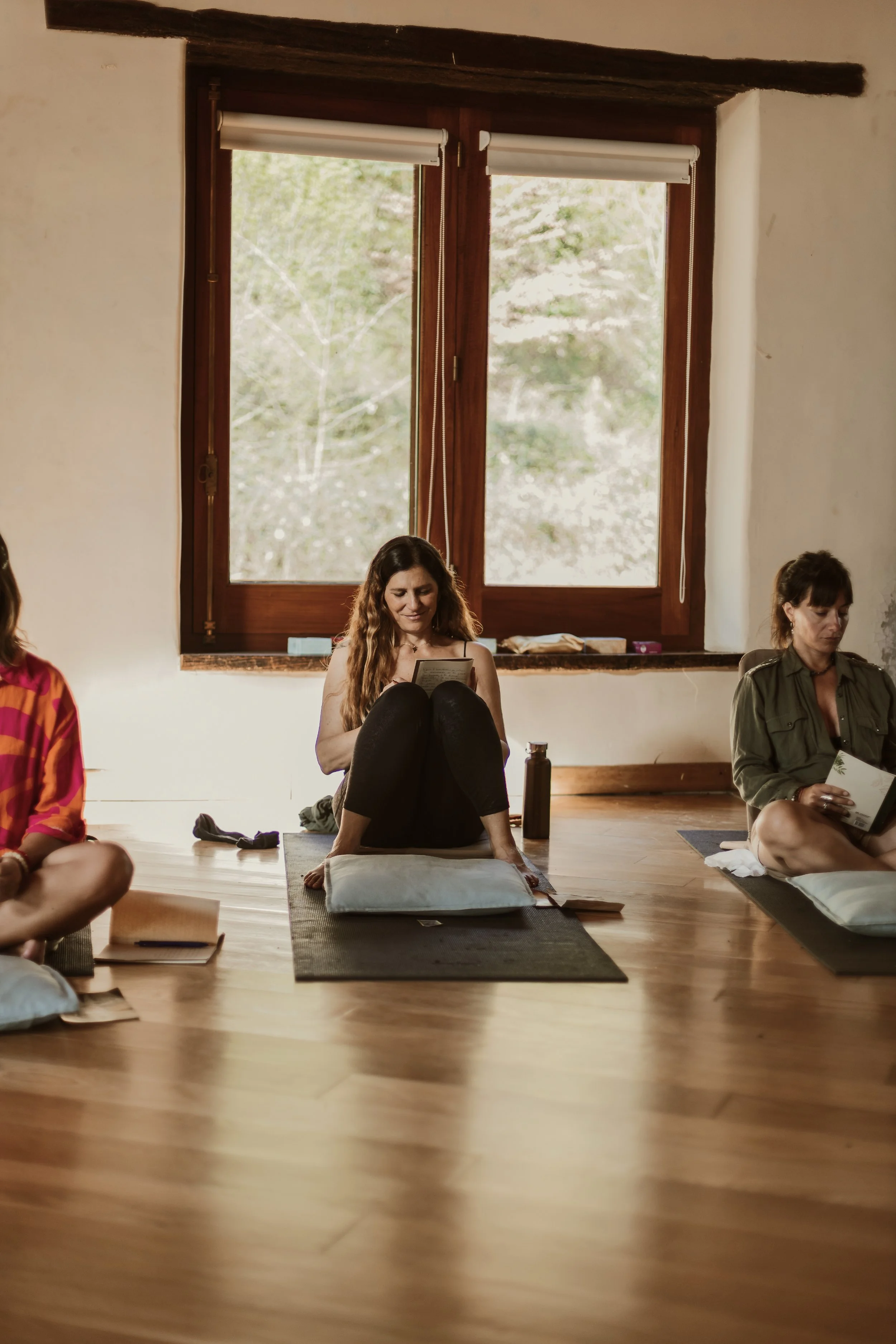 Grupo de personas participando en una clase de yoga o meditación en una habitación con paredes blancas y ventanas de madera.
