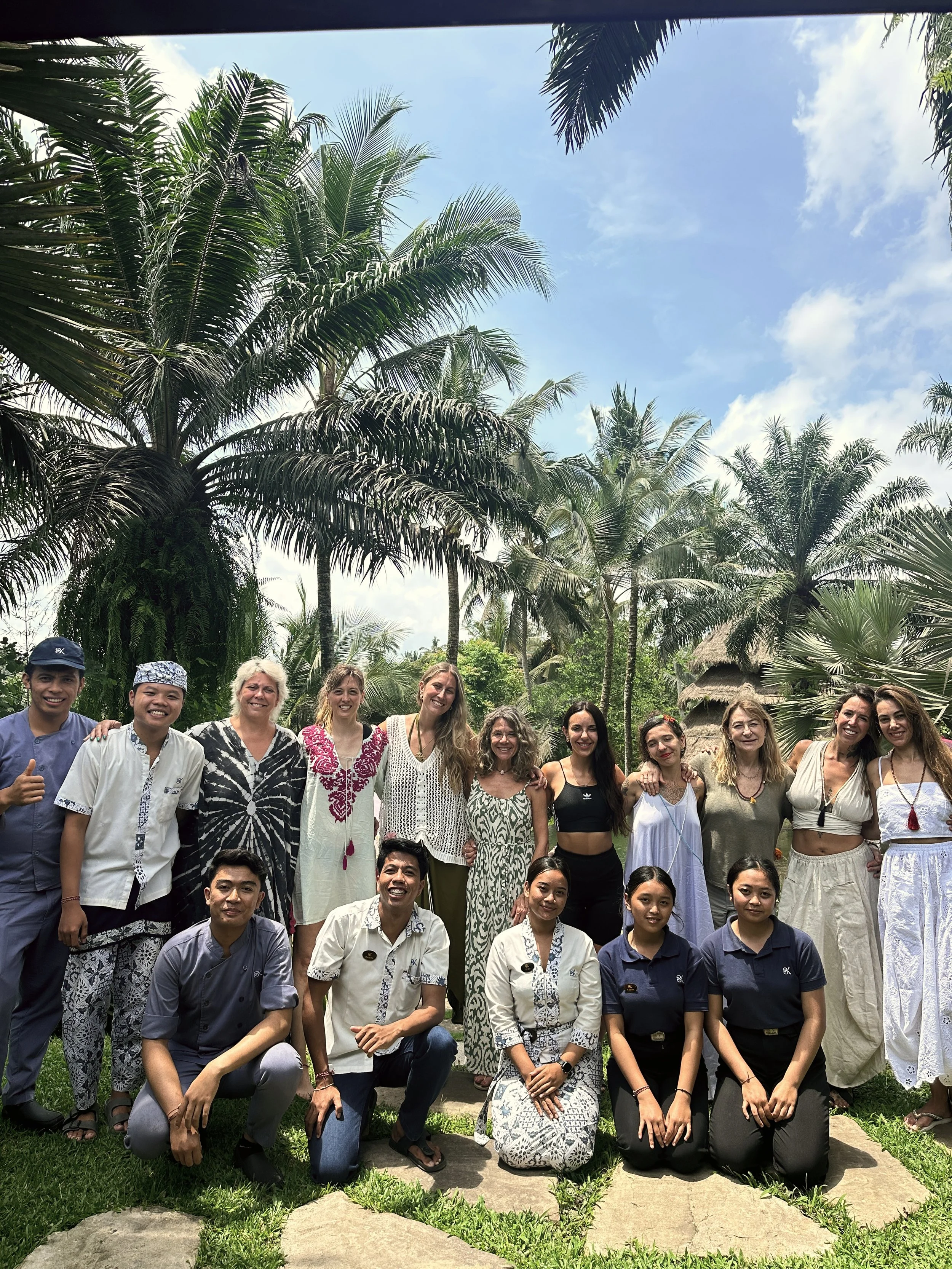 Grupo de personas en un jardín tropical con palmeras y cielo azul, posando para la foto.