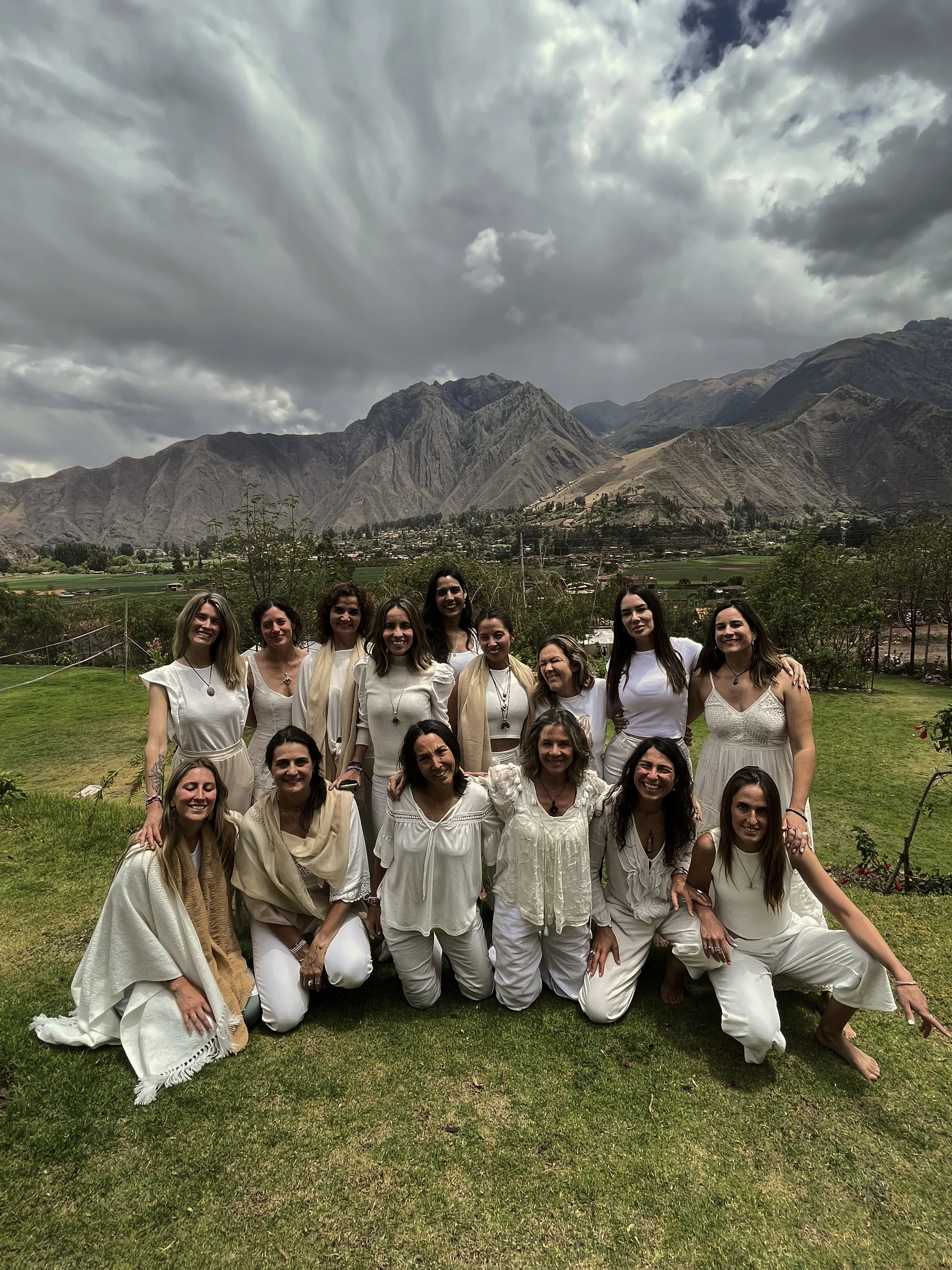 Grupo de mujeres vestidas de blanco en un campo con montañas y cielo nublado al fondo.