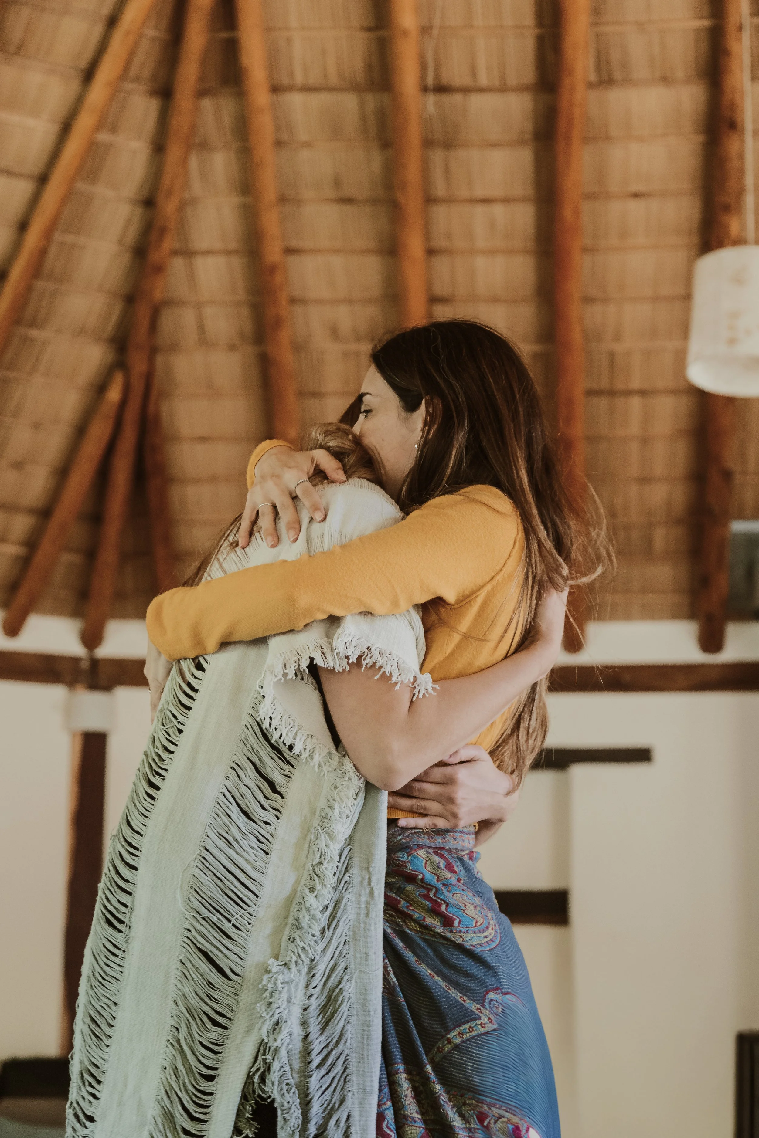 Dos mujeres abrazándose emotivamente en un espacio interior con techo de madera.