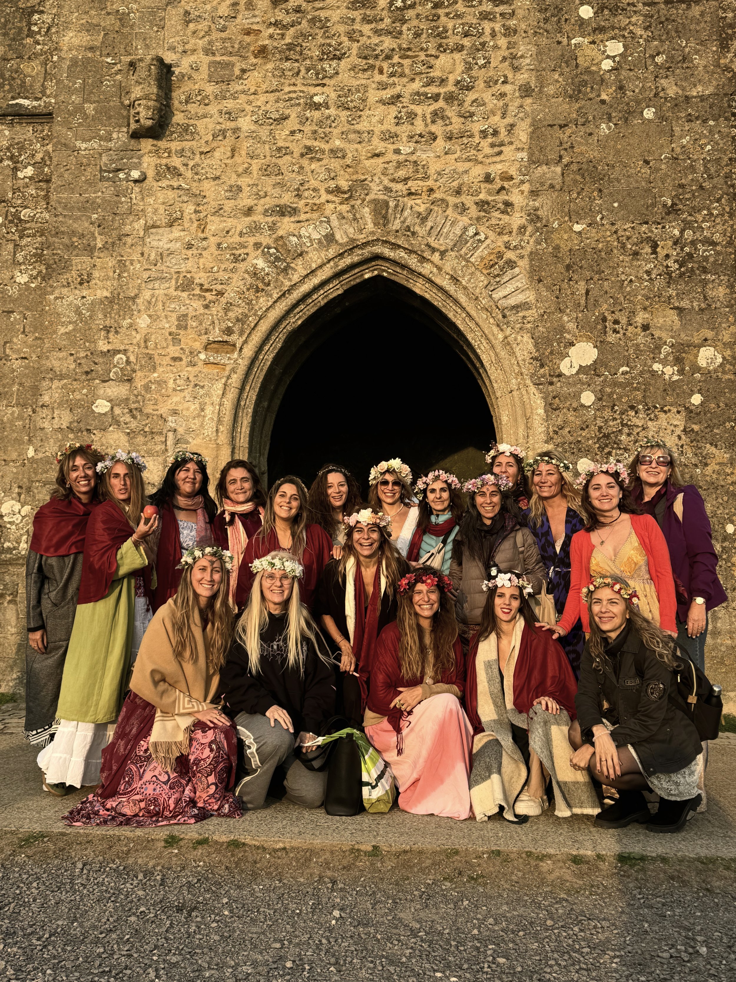 Grupo de mujeres con coronas de flores posando frente a una iglesia antigua.