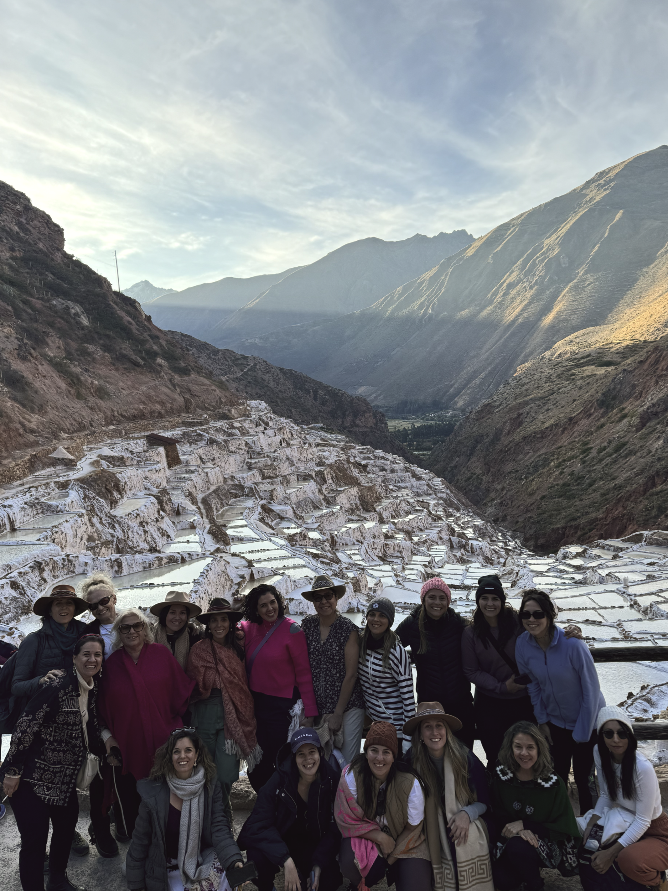 Grupo de personas posando en las terrazas de sal de aguas termales en un paisaje montañoso.