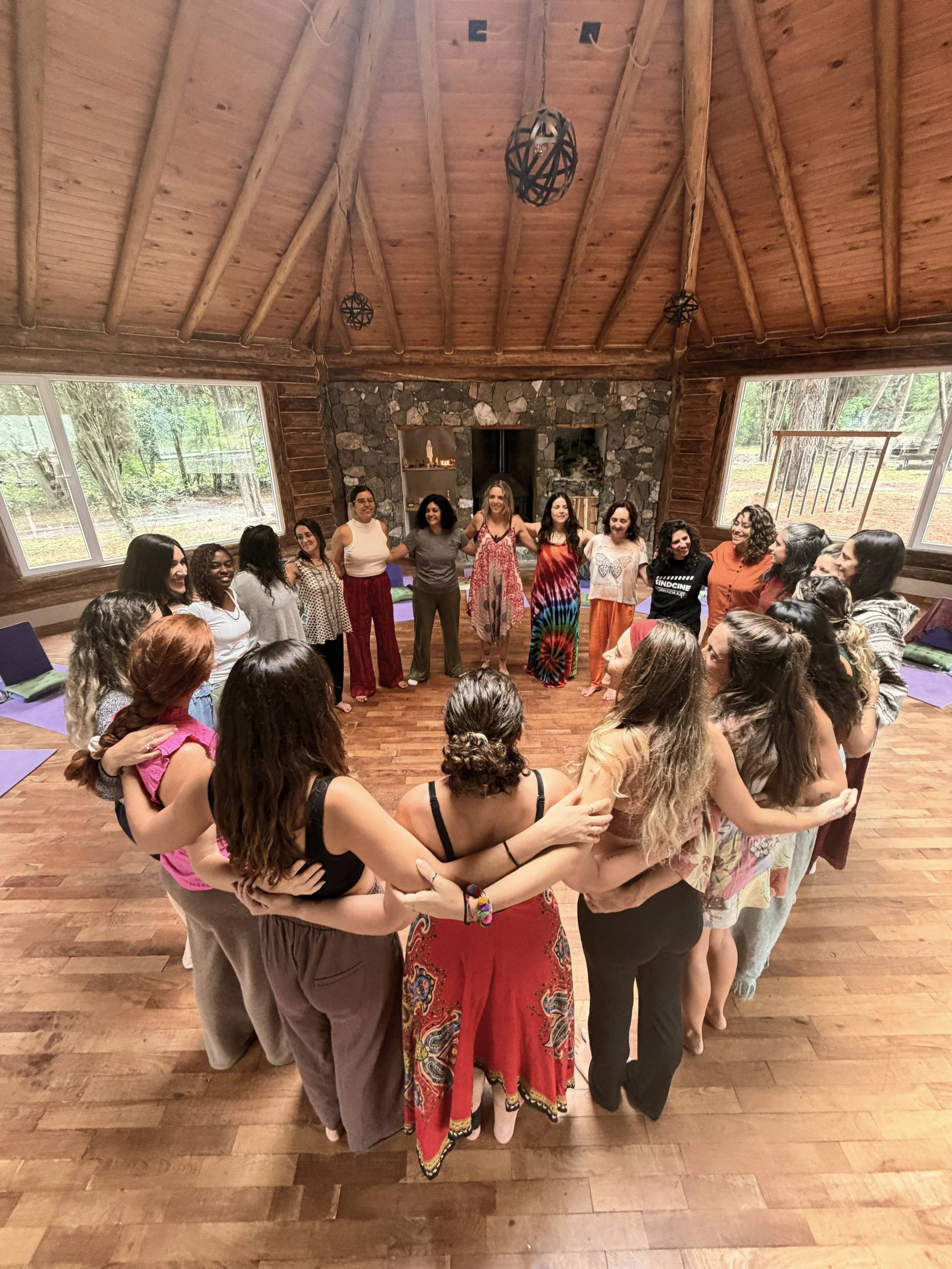 Grupo de mujeres formando un círculo en una sala de madera, compartiendo una actividad en conjunto.
