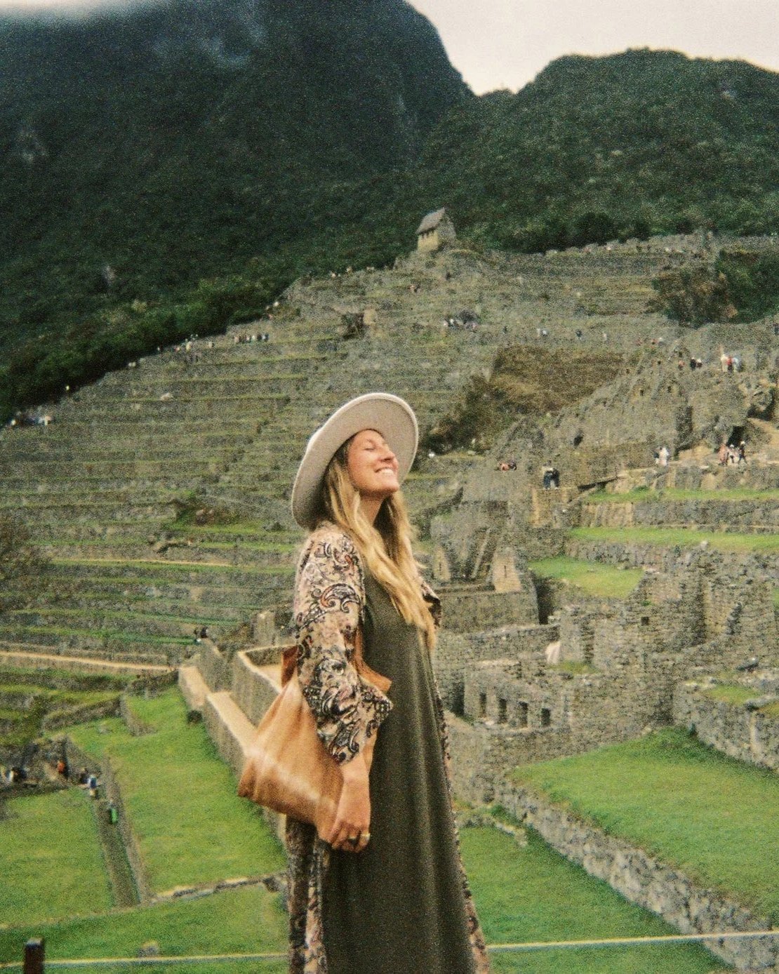 Mujer sonriendo y posando con las ruinas de Machu Picchu en el fondo.
