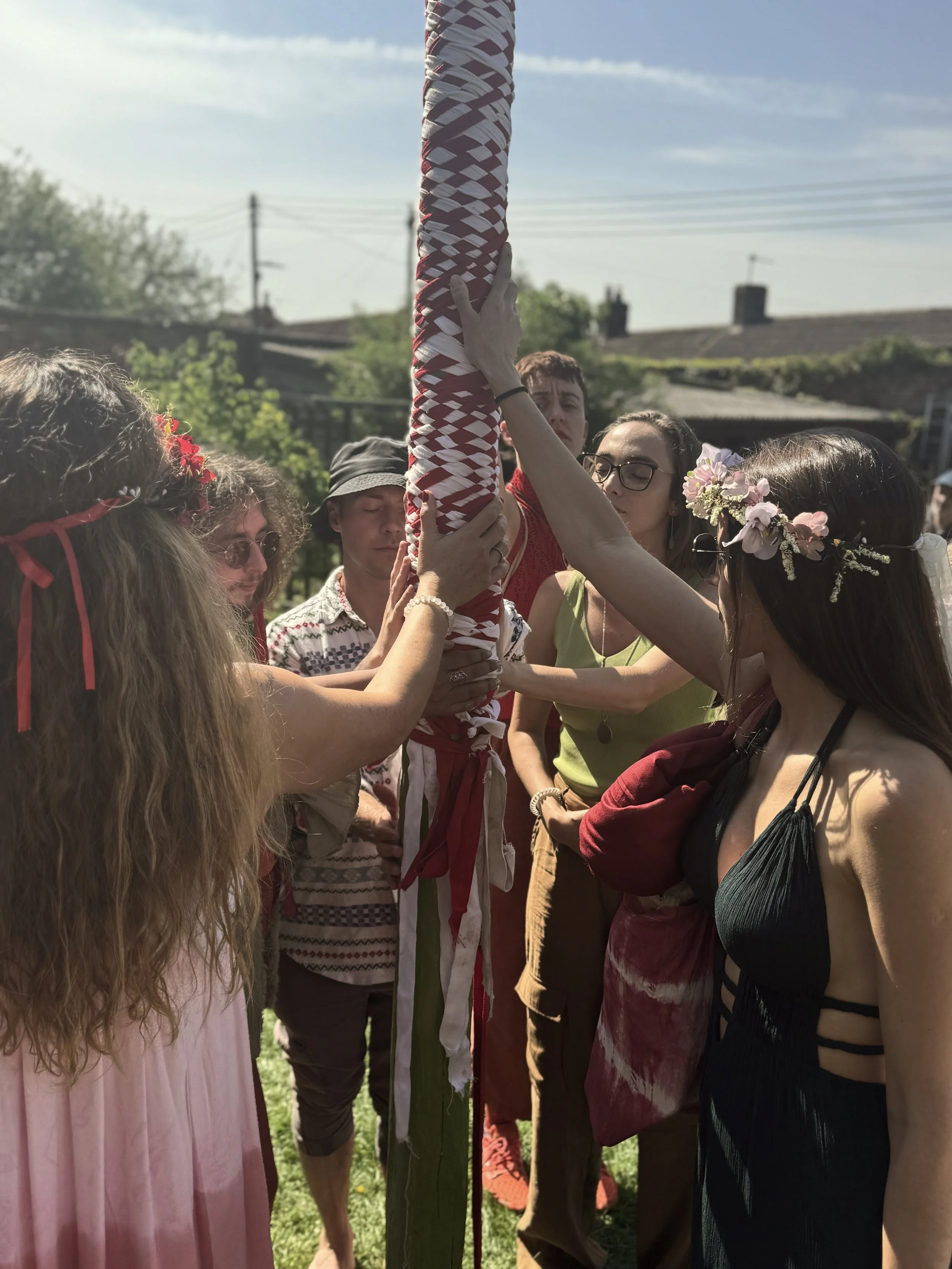 Grupo de personas participando en una ceremonia al aire libre, envolviendo un poste decorado con cintas de colores.