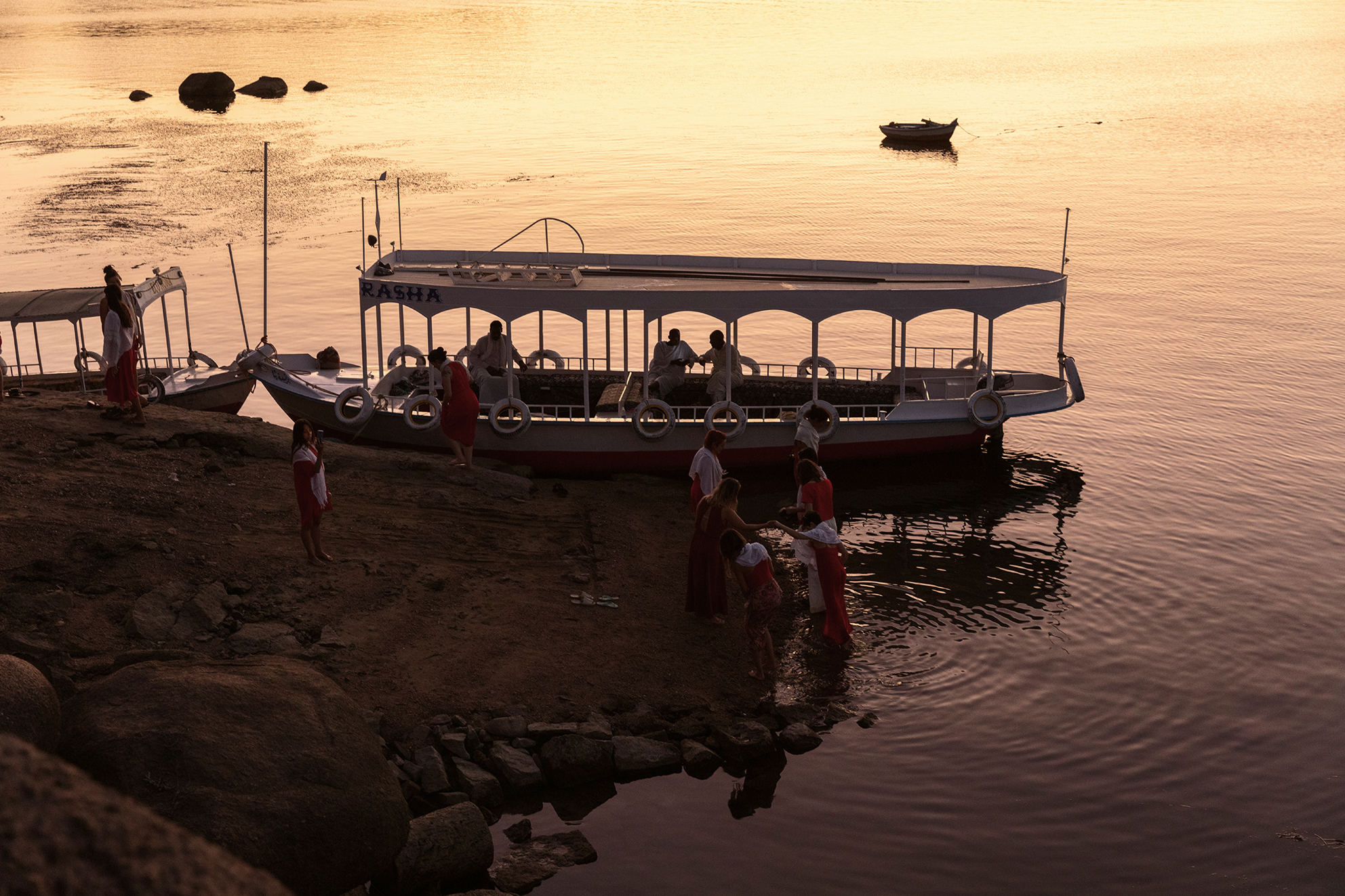Gente en el muelle junto a botes sobre aguas tranquilas al atardecer