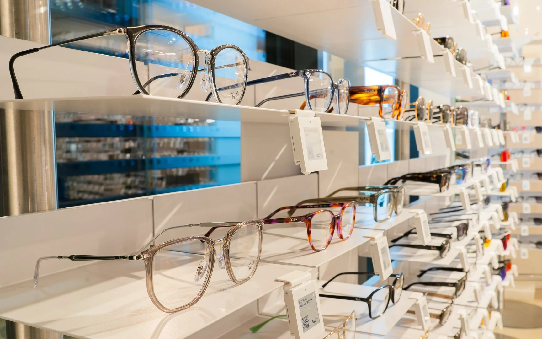 Výstava dioptrických okuliarov na bielych policiach v očnej optike.