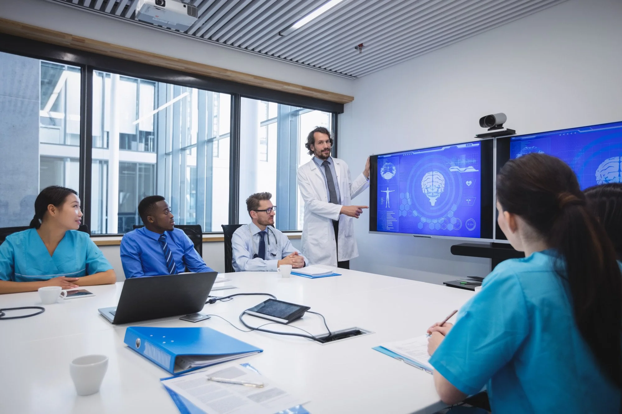 Medical professionals in a conference room attending a presentation about brain health with a doctor pointing at a digital screen.