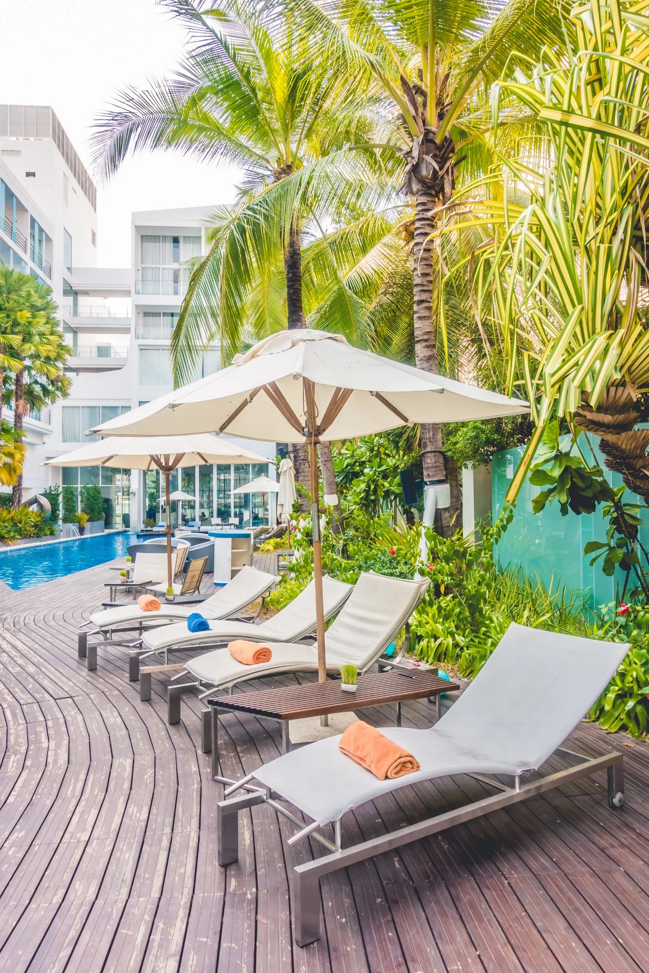 Poolside lounge chairs with rolled towels and umbrellas at a tropical resort.