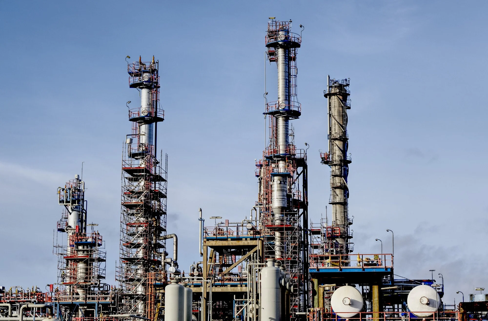 Industrial oil refinery with multiple tall distillation towers and equipment against a cloudy sky.
