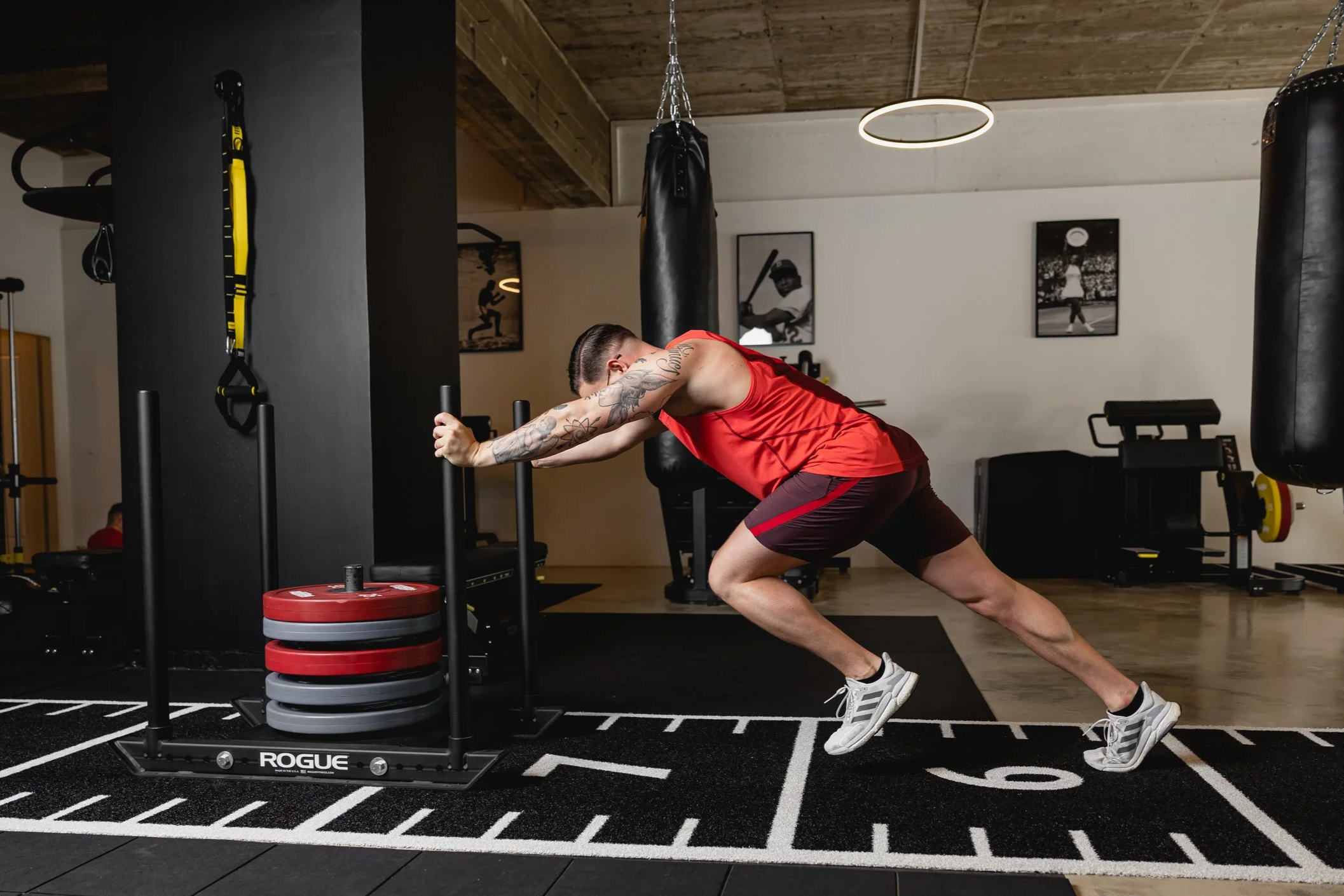 Mann beim Sled Push Workout im Fitnessstudio, gegen eine Gewichtswagen schiebend.